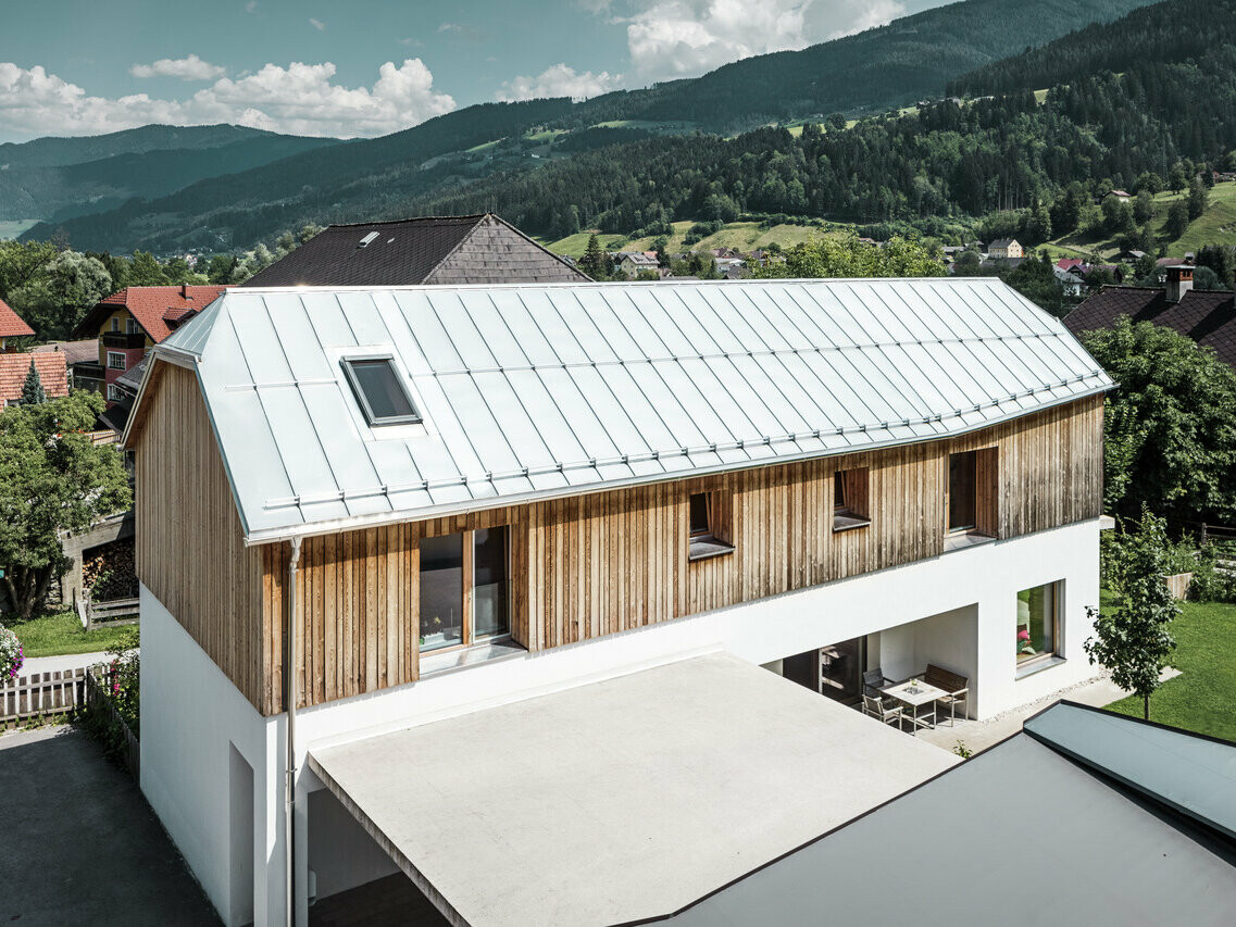 Vue de côté de cette maison familiale modern dans la jolie ville de Pruggern. Le toit a été rénové grâce au PREFALZ dans la teinte aluminium naturel.