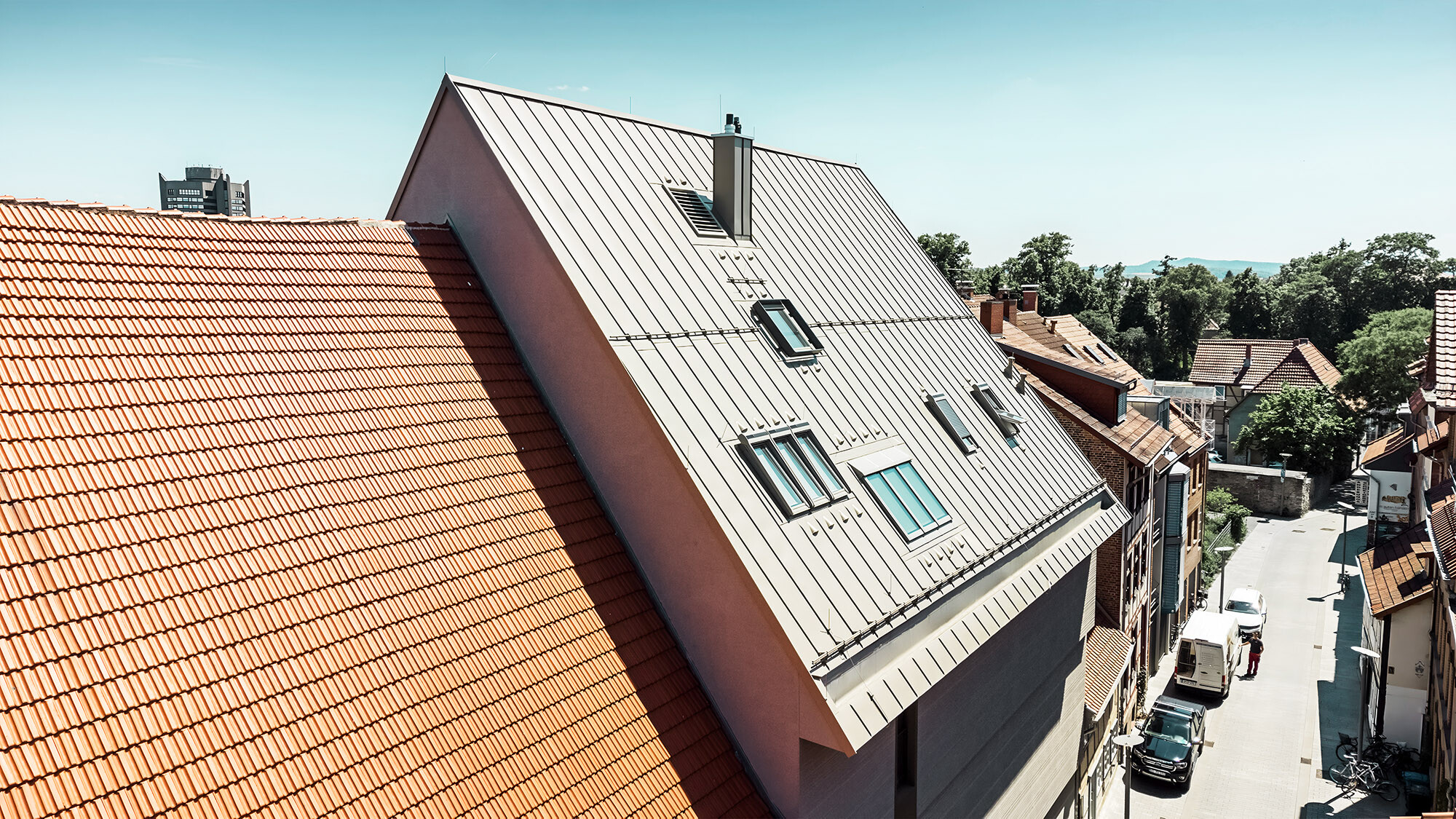 Une vue latérale de ce toit exceptionnel, à côté de constructions en tuiles plates de couleur rouille.