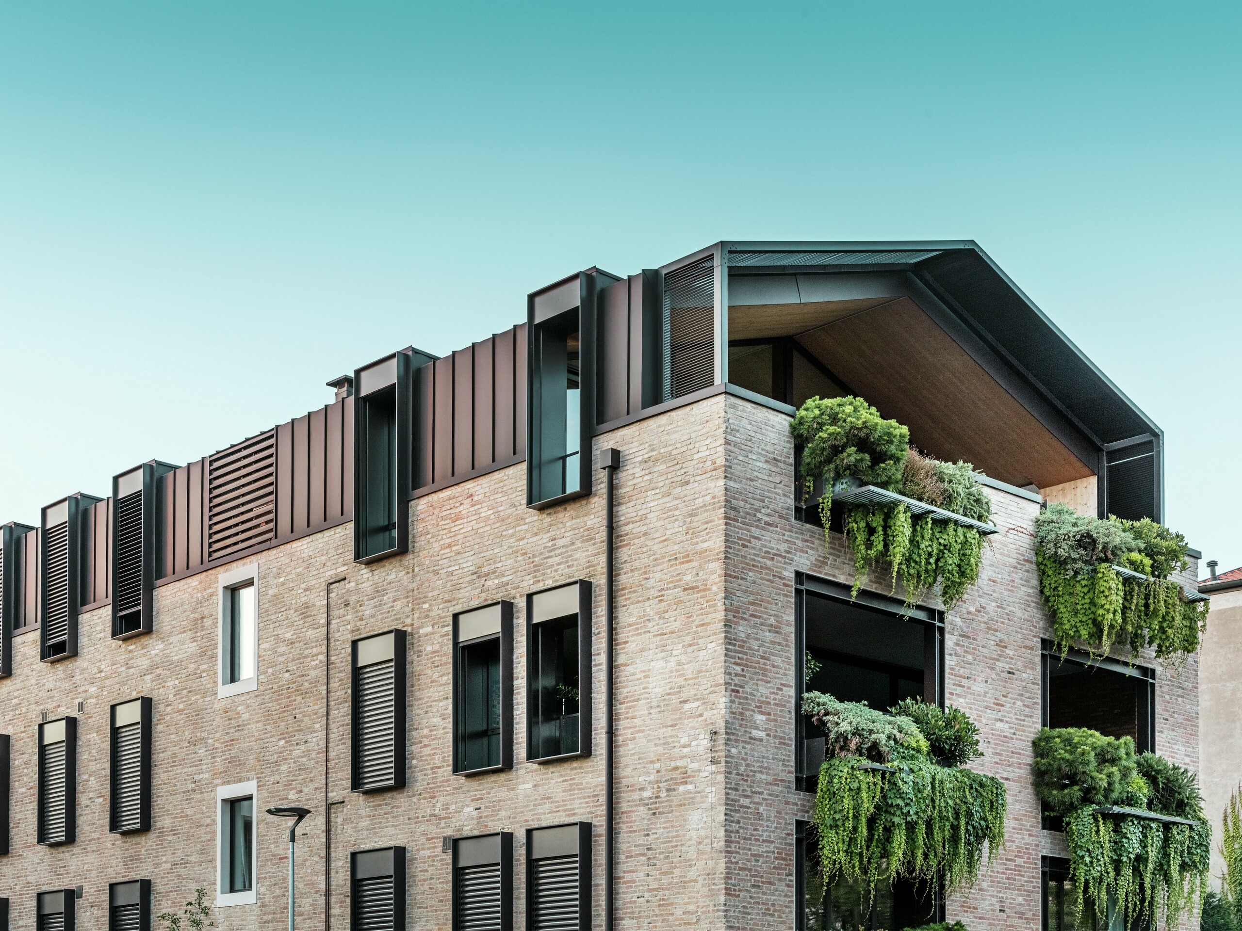 Maison durable en Italie avec toiture en aluminium PREFALZ en P.10 brun noisette et jardins suspendus sur la façade sud – architecture climatique active avec briques et végétalisation.