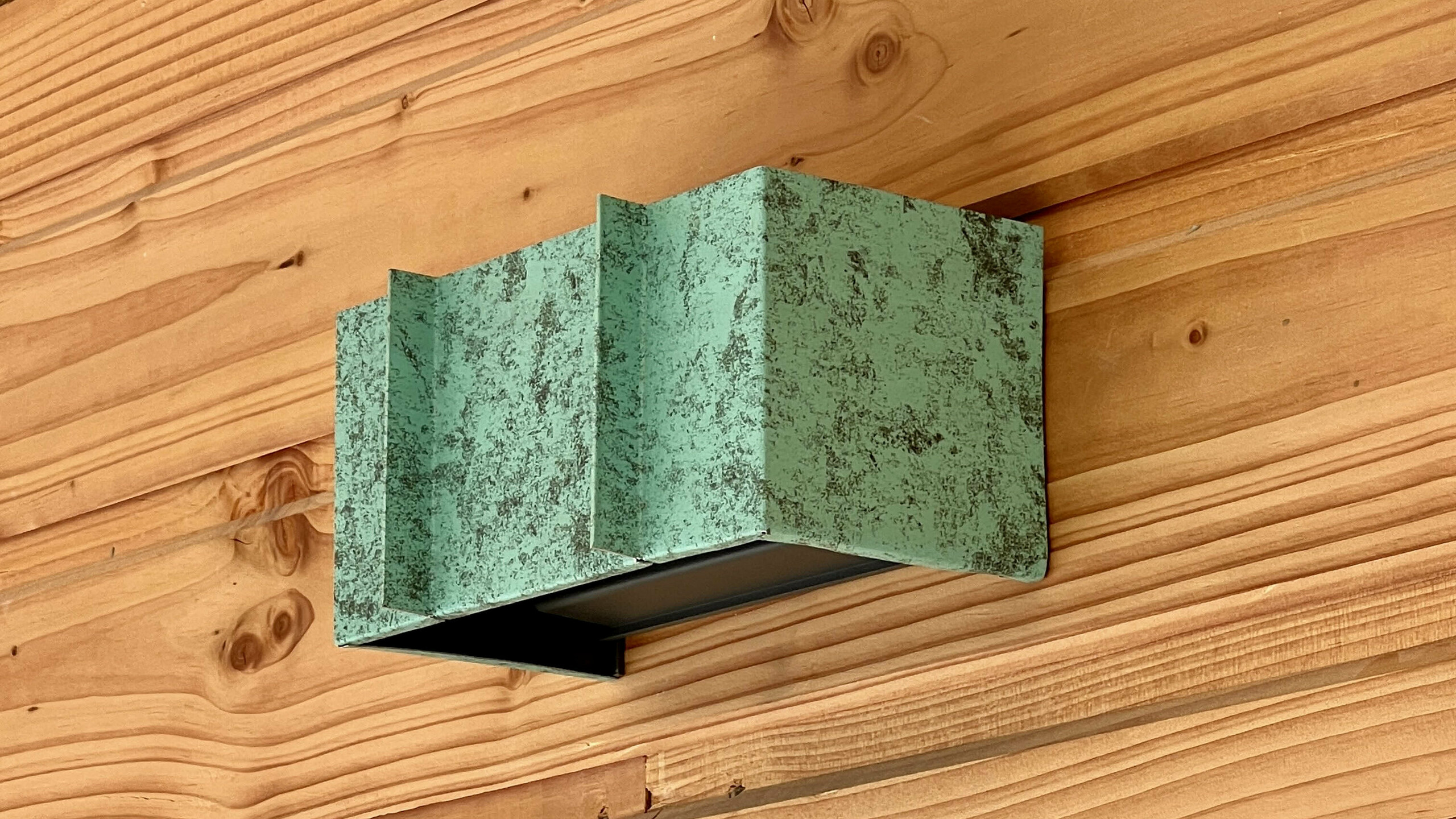 Zoom sur ce luminaire réalisé en aluminium Prefalz dans la teinte P.10 vert-de-gris pour être raccord avec la teinte de la couverture, celui-ci est posé sur une façade en bois