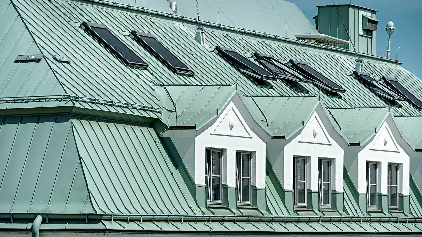 Nahaufnahme des Prefalz-Daches in P.10 patinagrün. In Mitten des Daches stechen drei weiße Dachfenstergauben hervor.