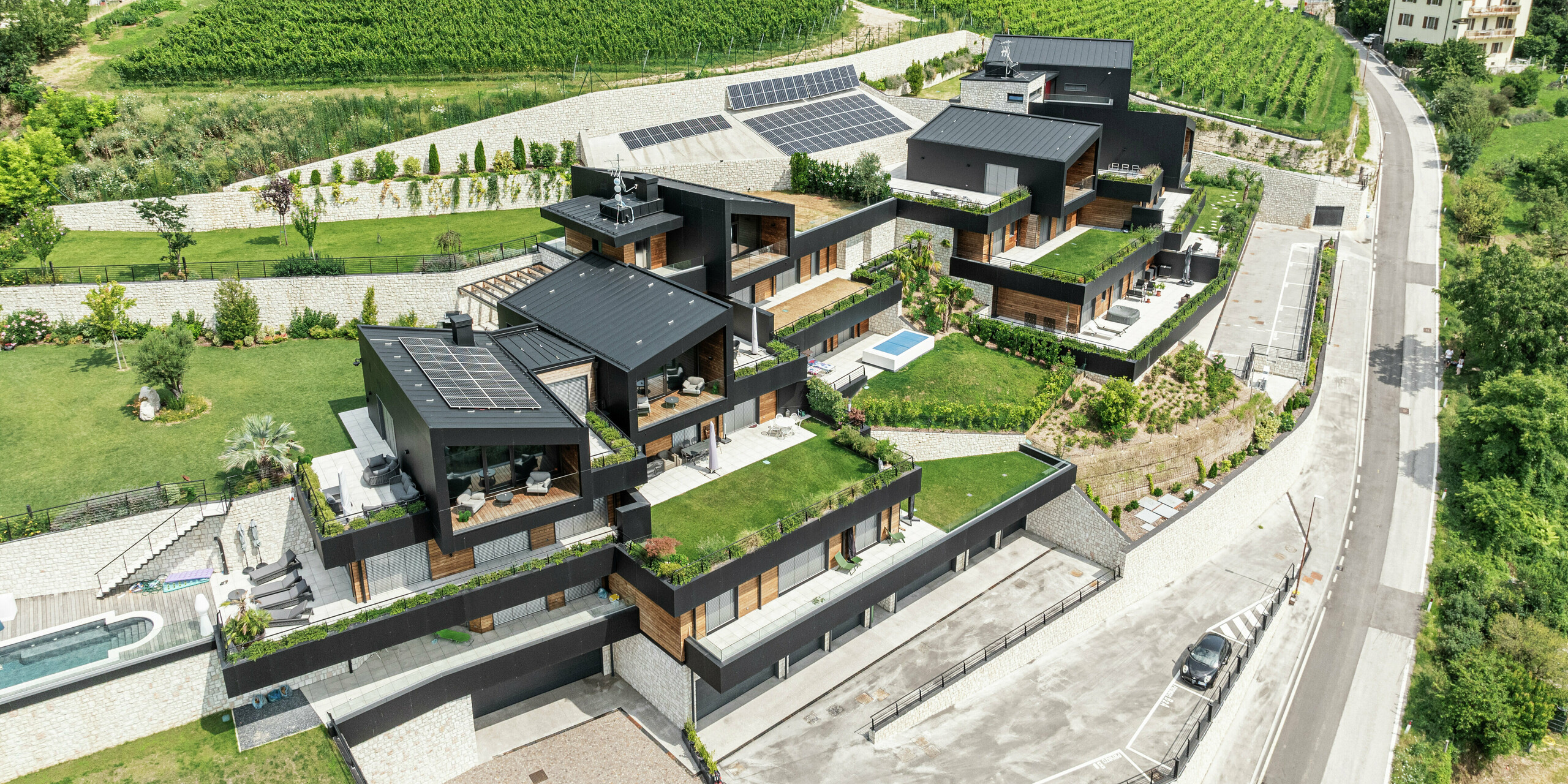 Niché dans le paysage vallonné pittoresque de Trente, ce complexe résidentiel exclusif allie construction durable et design moderne. Les façades en panneaux composites en aluminium PREFA en P.10 Noir et les toits en PREFALZ offrent une protection maximale contre les intempéries et garantissent une apparence élégante et durable. Des terrasses spacieuses, des plantes bien entretenues et des systèmes photovoltaïques soulignent le concept respectueux de l'environnement. L'intégration harmonieuse dans la nature ainsi que les détails luxueux tels que les piscines privées et les jardins soignés font de ce projet résidentiel un lieu de bien-être unique.