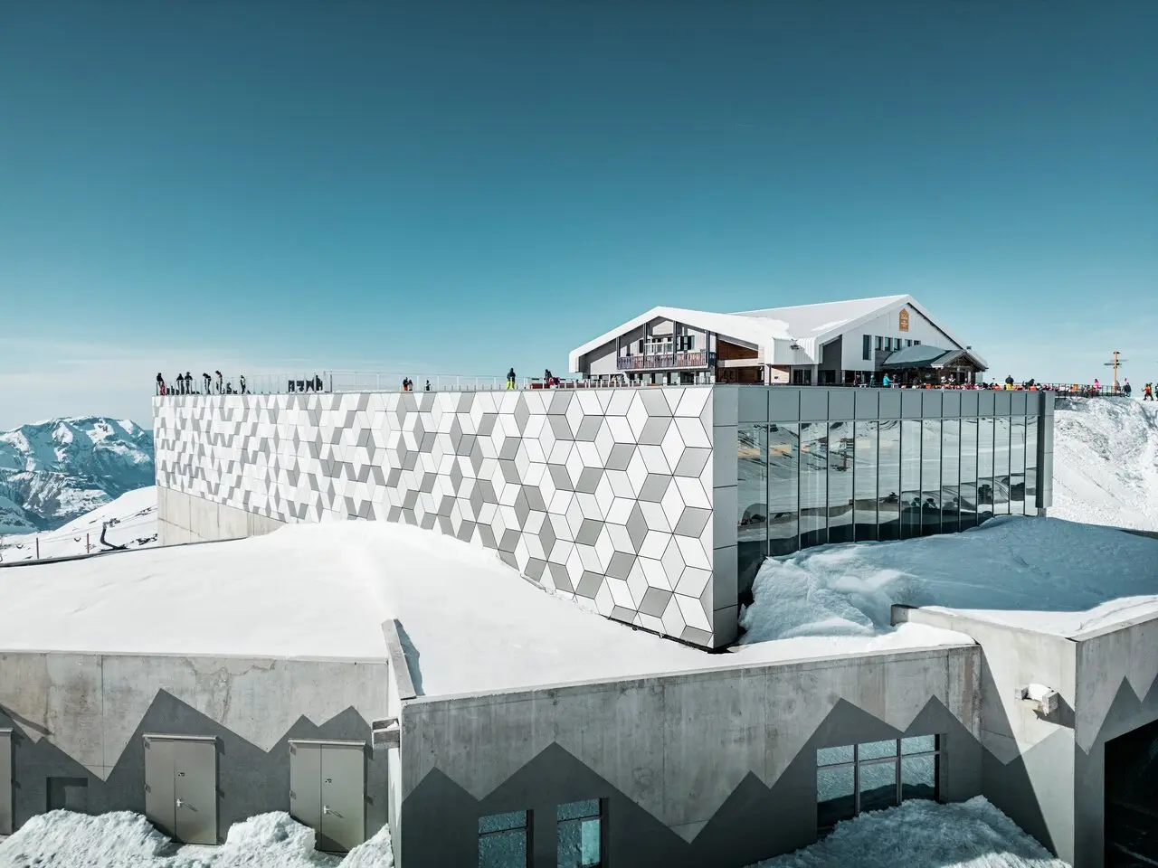 Vue d'une des stations du nouveau téléphérique Le Jandri de la station Les 2 Alpes, recouverte de panneaux composites en aluminium PREFABOND façonné en losanges de trois couleurs différentes : blanc Prefa, blanc pur et argent fumé.