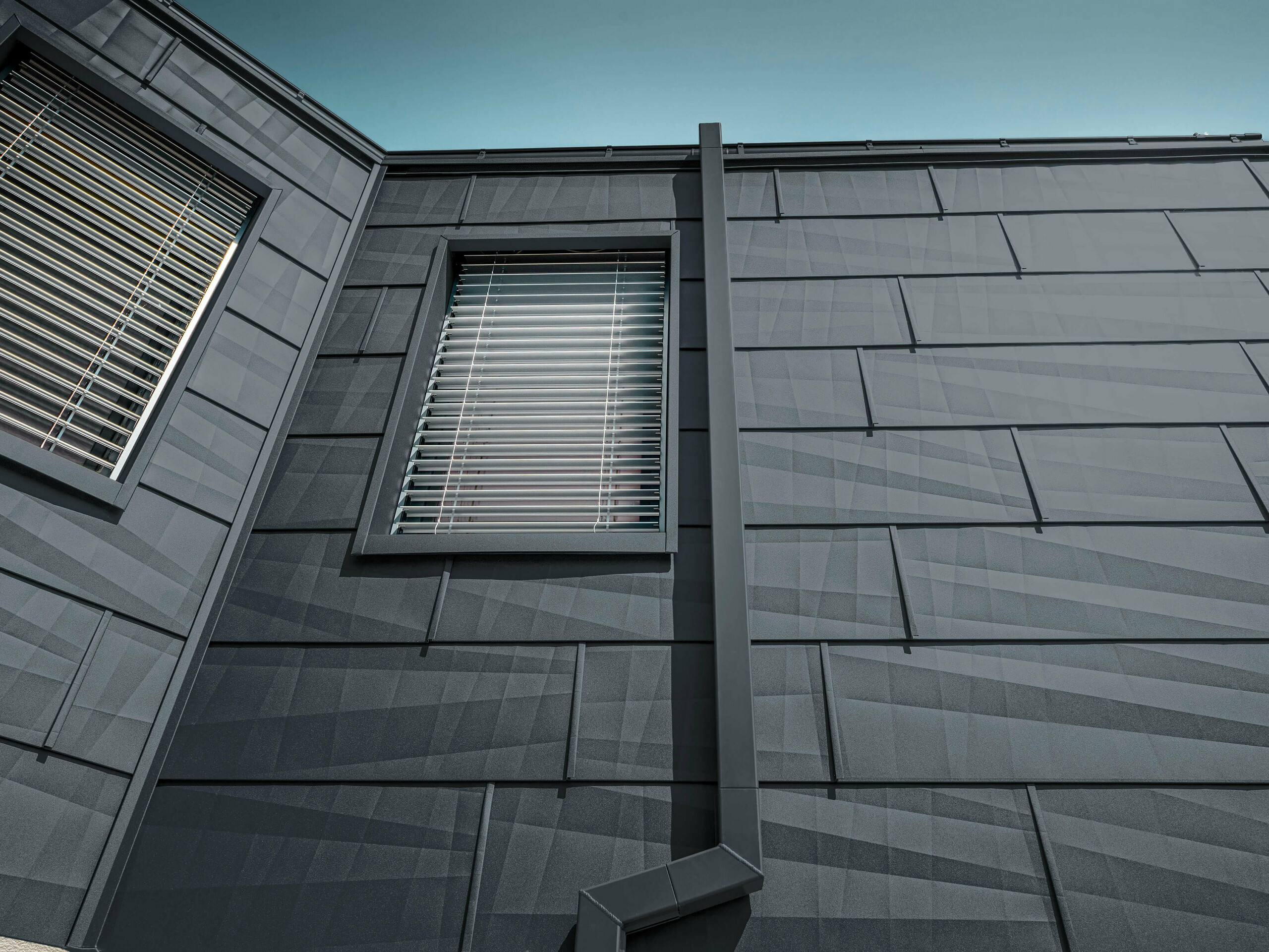 Façade revêtue du panneau de façade FX.12 PREFA couleur anthracite, panneauxen ’aluminium sur la façade avec tuyau de descente carré couleur anthracite de PREFA.