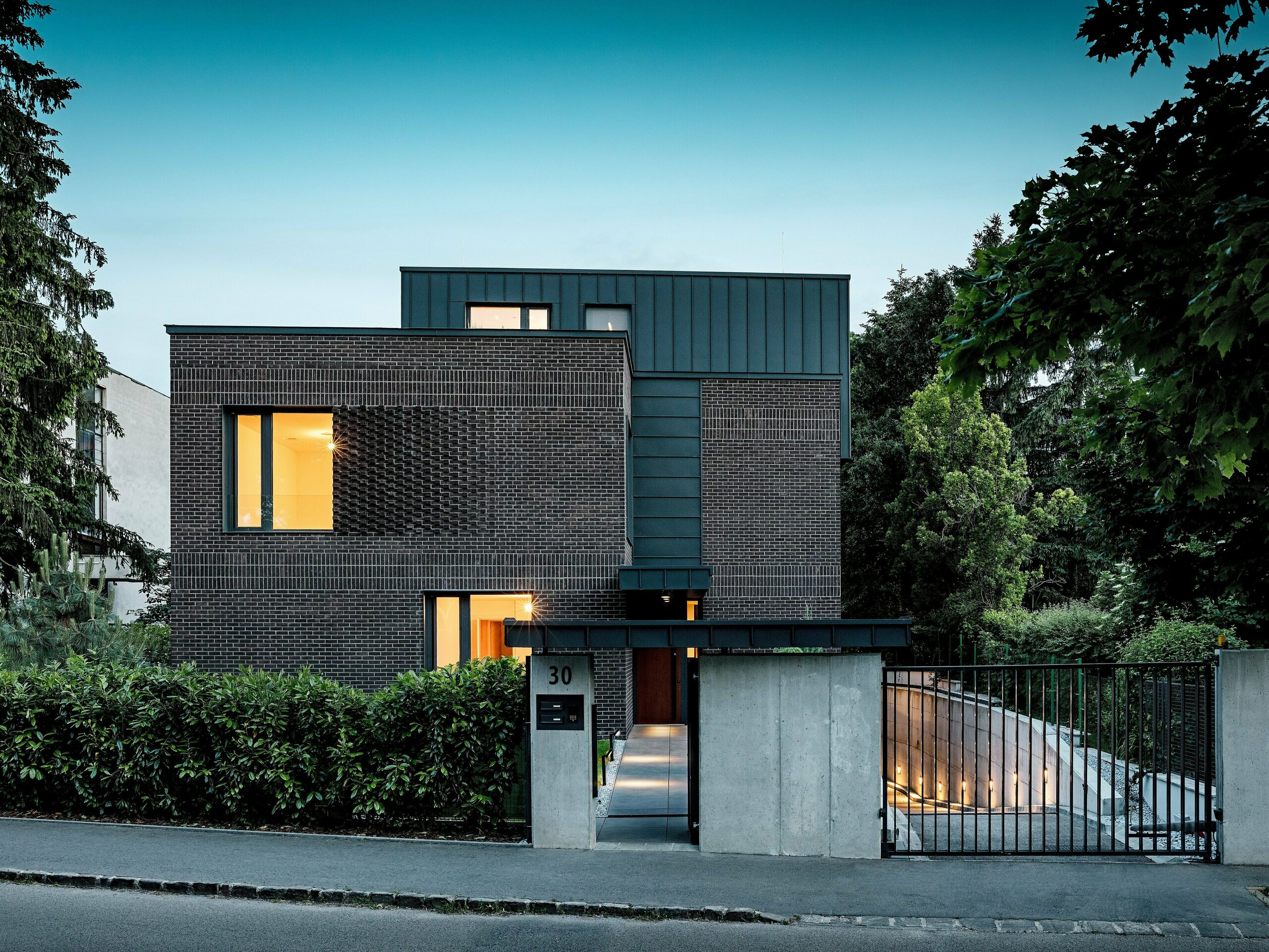 L'image présente un immeuble d'appartements moderne à Budapest, dont la toiture cubique, revêtue d'aluminium PREFALZ P.10 anthracite, contraste de façon saisissante avec le paysage historique environnant. Les joints verticaux créent un jeu de lumière captivant et soulignent la pureté des lignes architecturales. Les produits en aluminium PREFA, de haute qualité, confèrent au bâtiment une élégance intemporelle, tout en impressionnant par leur durabilité, leur résistance aux intempéries et leur finition impeccable. La façade et la toiture anthracite attirent immédiatement le regard et mettent en valeur le caractère novateur du bâtiment.