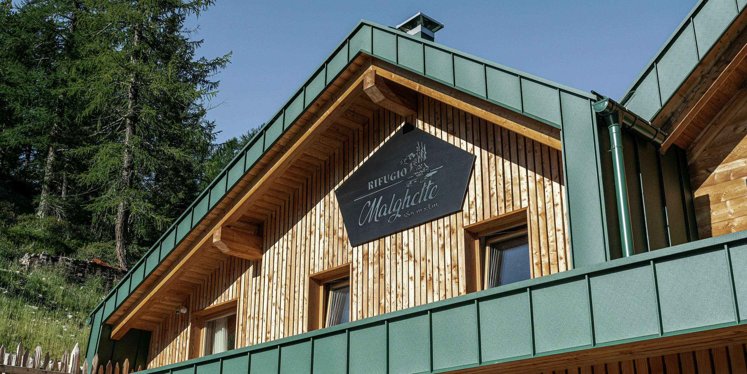 Vue détaillée de la façade du Rifugio Malghette avec PREFALZ en P.10 Vert Mousse - durable, sans entretien et parfaitement combiné avec le bois naturel. Le revêtement en aluminium durable protège de manière fiable la cabane des conditions météorologiques extrêmes des altitudes alpines.