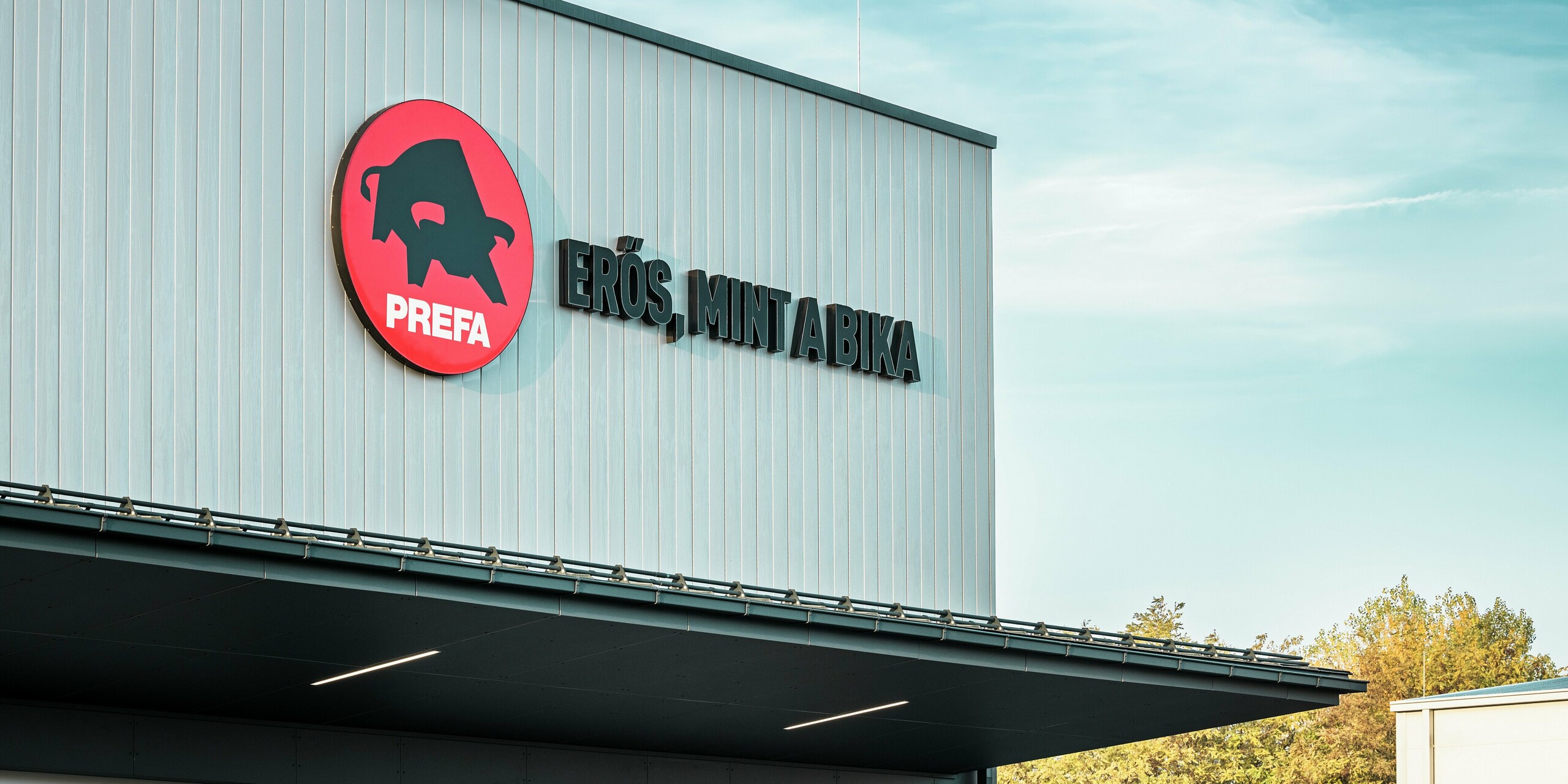 Le logo PREFA frappant et le slogan hongrois « Erős, mint a bika » (« Robuste comme un taureau ») caractérisent la façade du site PREFA à Törökbálint. Le revêtement avec des Sidings PREFA en argent métallisé assure un look moderne, une résistance maximale aux intempéries et une durabilité. La finition précise souligne les normes de qualité élevées de PREFA et reflète la force de la marque.