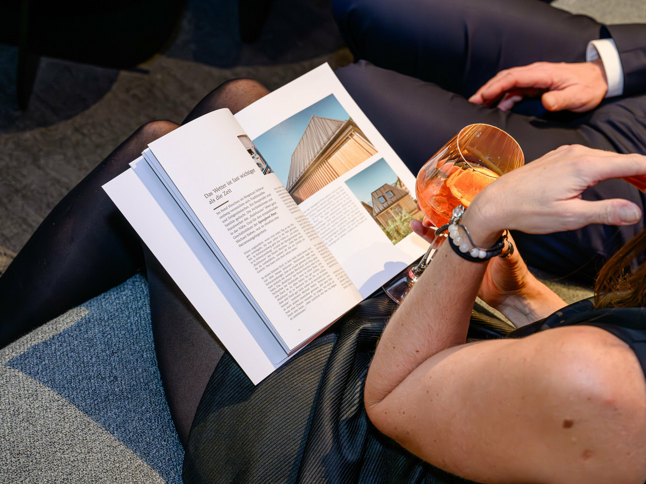 Une scène d'ambiance de la présentation PREFARENZEN 2026 au k47.wien : une femme élégante, un verre à la main, feuillette le nouveau livre d'architecture PREFA, un ouvrage captivant regorgeant d'inspiration. On aperçoit un bâtiment intégrant PREFALZ, mettant en valeur le caractère moderne de l'aluminium. L'image évoque le plaisir, le partage et une soif d'innovation. La surface haut de gamme de PREFA allie esthétique et durabilité, idéale pour concrétiser des idées architecturales créatives. L'aluminium PREFA établit de nouvelles normes et inspire les professionnels tels que les urbanistes, les architectes et les fabricants.