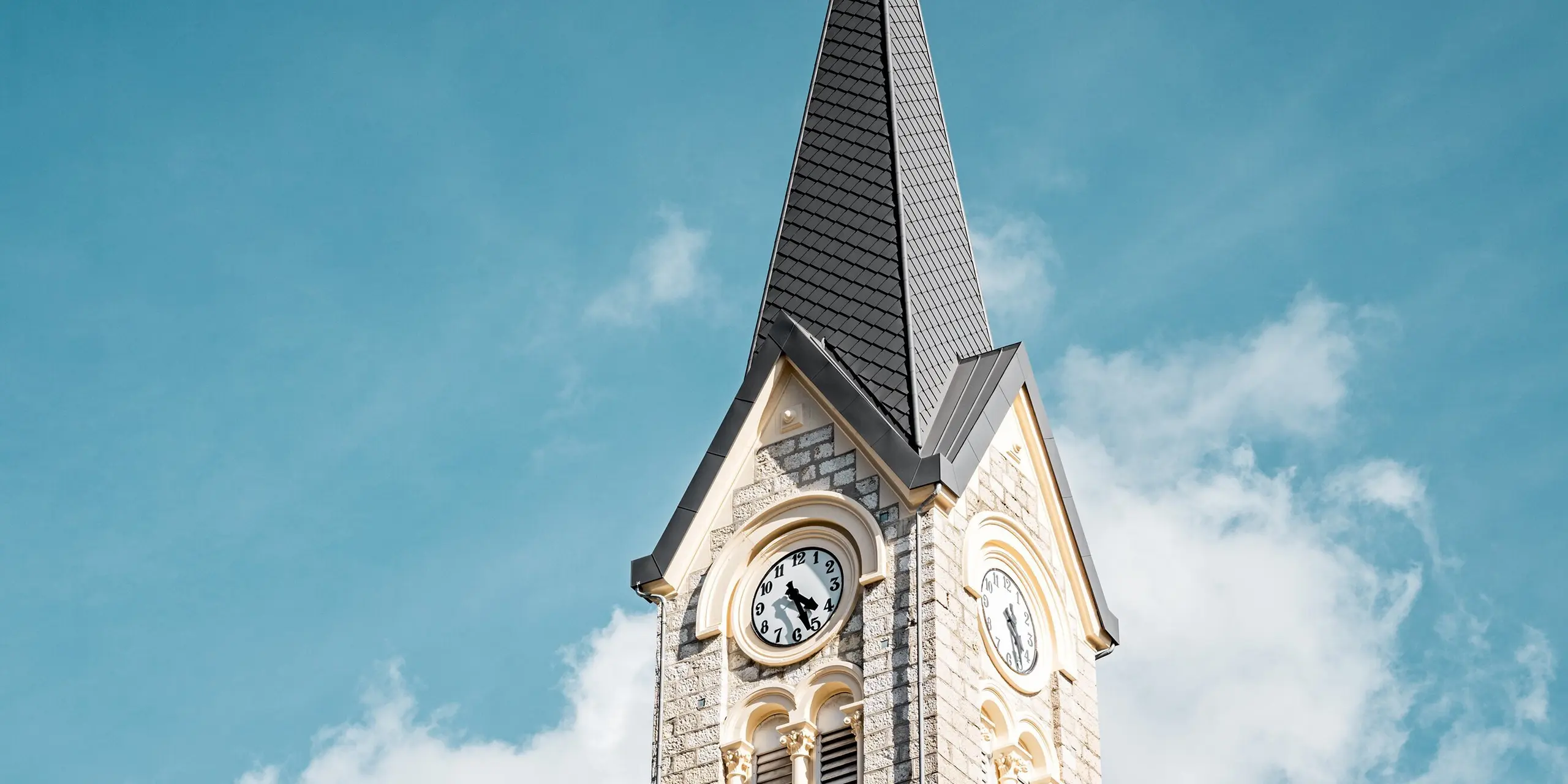 Vue détaillée du clocher rénové de l'église du Sentier, en Suisse, avec sa flèche élancée et impressionnante, réalisée en losanges PREFA 29 x 29 cm, coloris P.10 Gris sombre. La toiture en aluminium, posée avec précision, souligne l'élégance de la tour et crée un contraste saisissant avec la pierre naturelle claire. L'aluminium PREFA se distingue par sa légèreté, sa grande résistance aux intempéries et sa protection durable, idéale pour les toitures exigeantes.