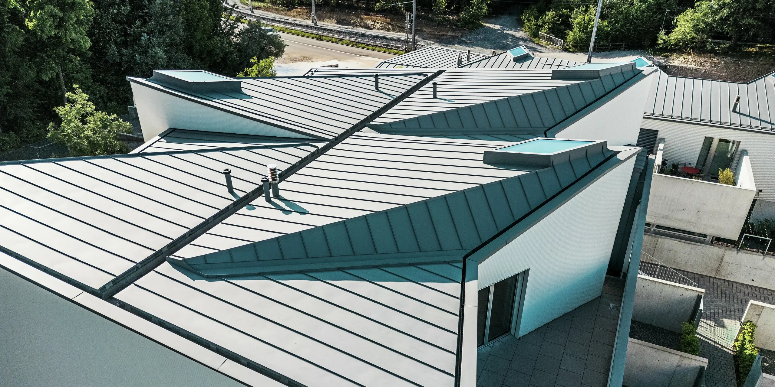 Géométrie de toiture spectaculaire avec PREFALZ gris quartz : les toitures à joints debout pliés des mini-maisons de Zollikerberg créent des effets architecturaux remarquables et des lignes épurées. La solution de toiture PREFA, de haute qualité, impressionne par sa durabilité, sa conception sans entretien et sa flexibilité – idéale pour les formes complexes dans des environnements exigeants comme ce site à flanc de colline, desservi par une voie ferrée.