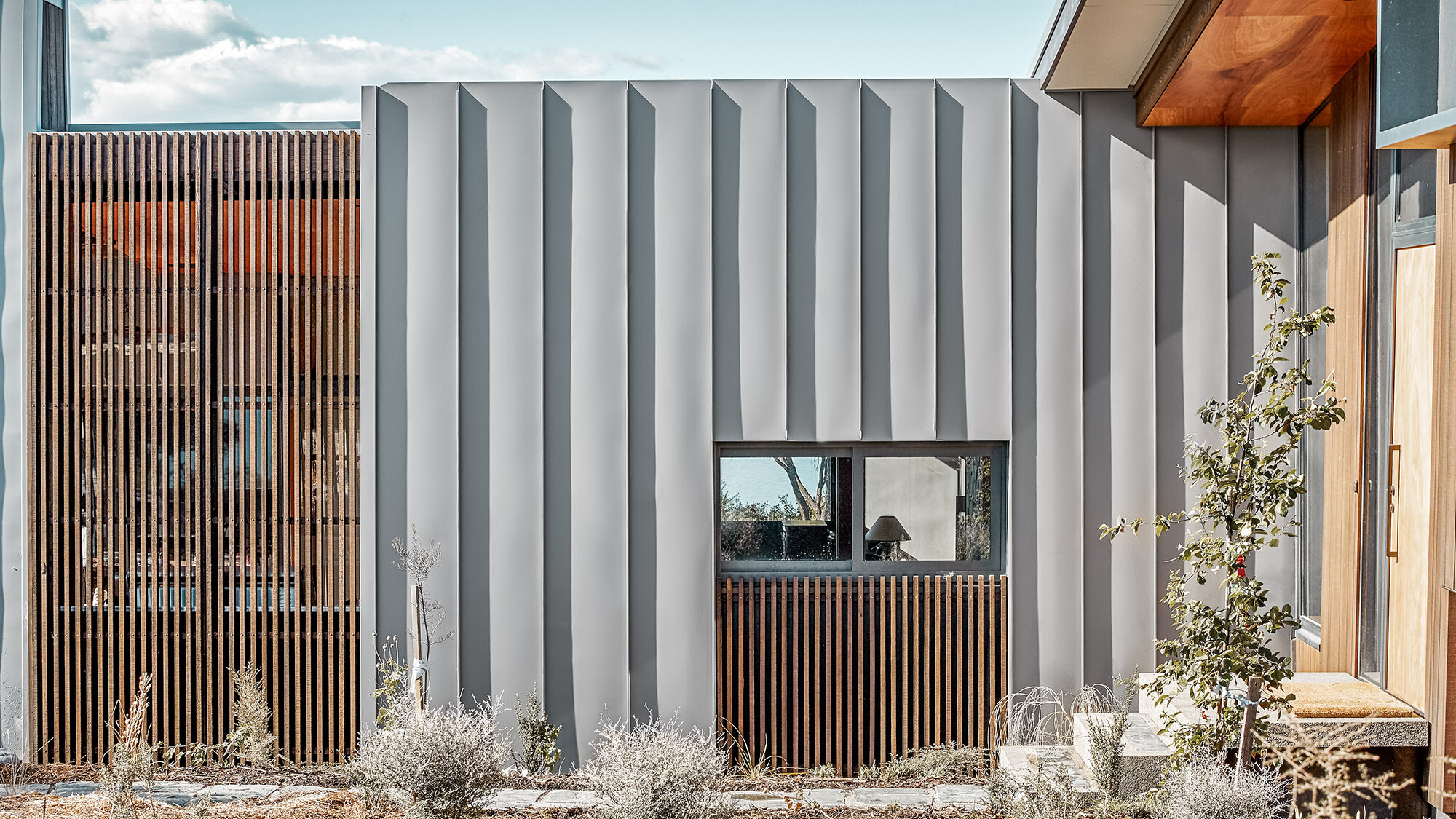 Eine Detailaufnahme des Einfamilienhauses mit Blick auf die Holz- und Aluminiumelemente der Fassade sowie in einen Teil des Interieurs.