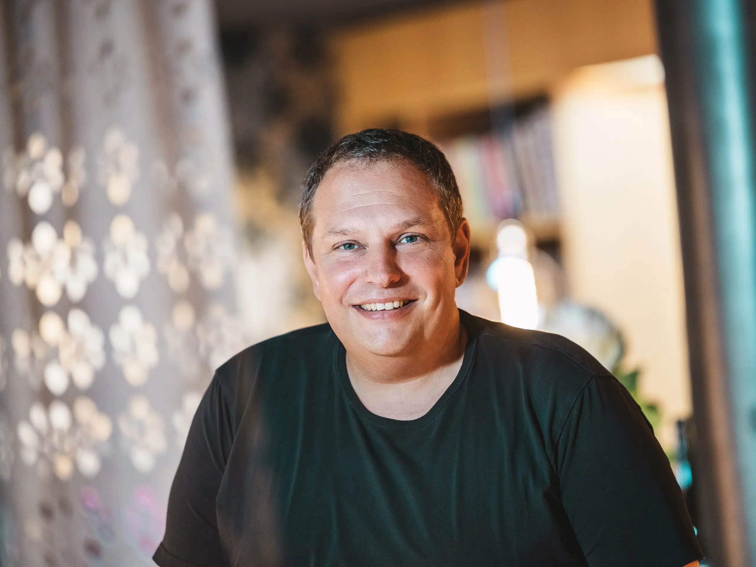 Portrait de l’architecte vorarlbergeois Jürgen Haller, qui a conçu la maison Immi à Ebnit comme une maison en bois résolument épurée et durable. L’architecte souriant se tient dans un intérieur baigné d’une lumière chaleureuse. Son projet associe des matériaux régionaux à une robuste toiture solaire PREFA composée de tuiles solaires et R.16 en P.10 noir, conçue pour résister aux conditions alpines.