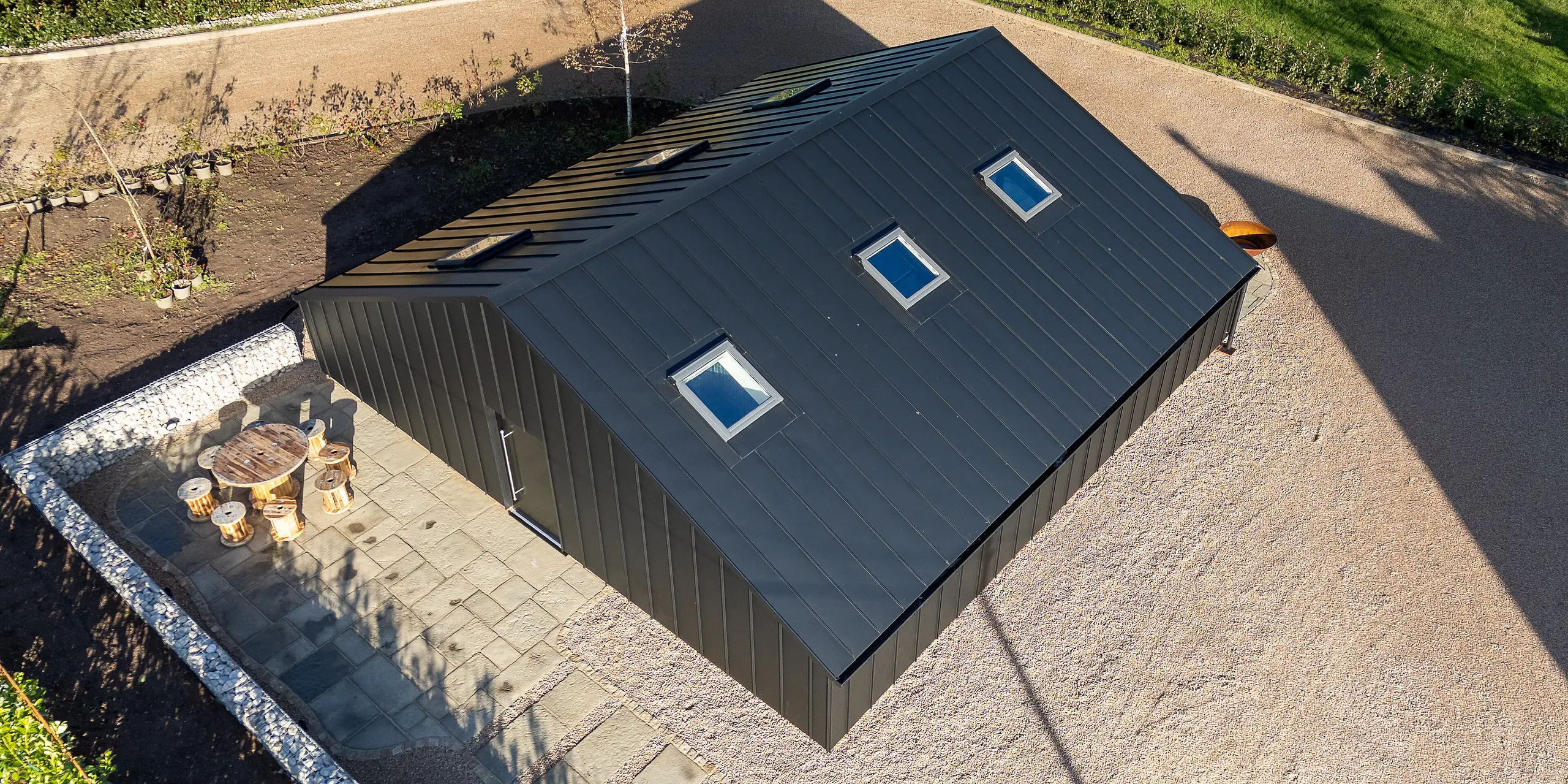 Vue aérienne d'un bâtiment de loisirs moderne à Ranton, revêtu d'une coque en aluminium PREFA P.10 Noir. La toiture PREFA, à la finition homogène et aux joints debout impeccables, intégrant des fenêtres de toit, souligne l'élégance architecturale. Robuste et résistante aux intempéries, la surface en aluminium garantit une stabilité durable et apporte une touche d'élégance au vaste espace extérieur.