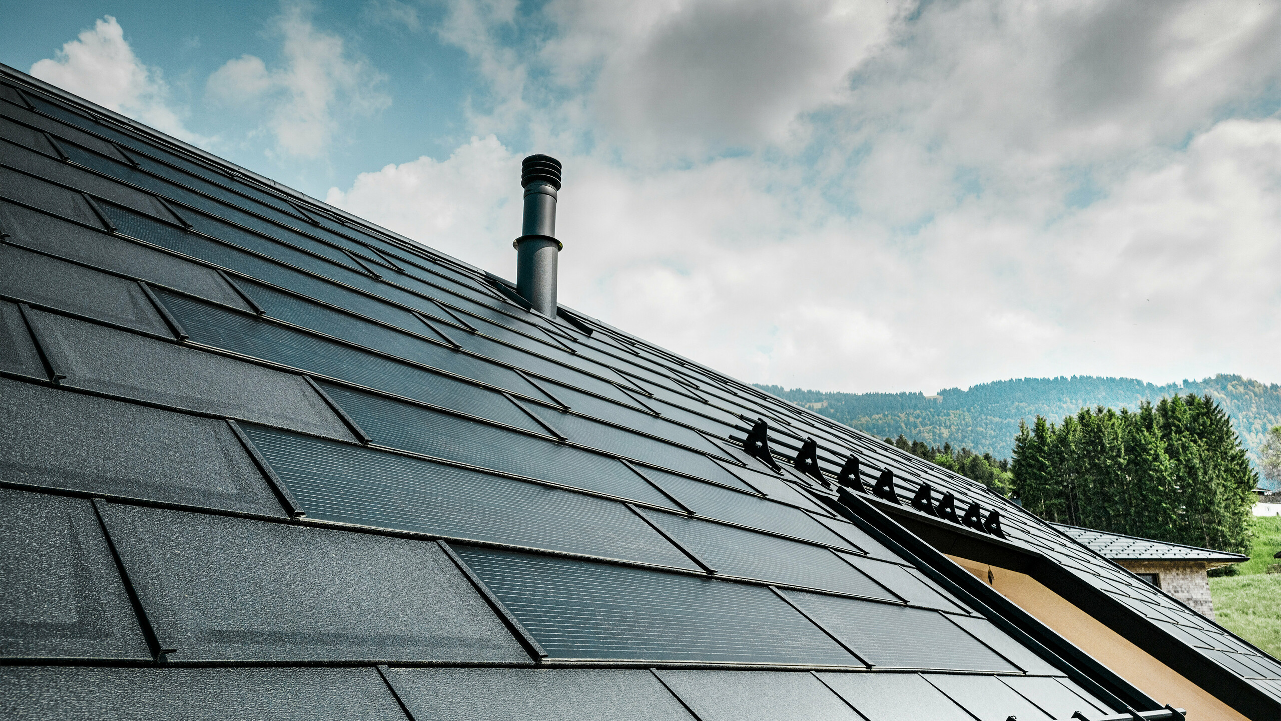 Vue détaillée de la tuile solaire PREFA combinée avec la tuile R.16 PREFA éprouvée, de couleur noire P.10, sur une maison écologique à Egg, en Autriche. Les modules photovoltaïques intégrés montrent l'alliance parfaite entre l'énergie renouvelable et un design de toit sophistiqué. Les plaques de toit noires R.16 avec le système de protection contre la neige complètent la surface esthétique du toit et assurent en outre la sécurité.