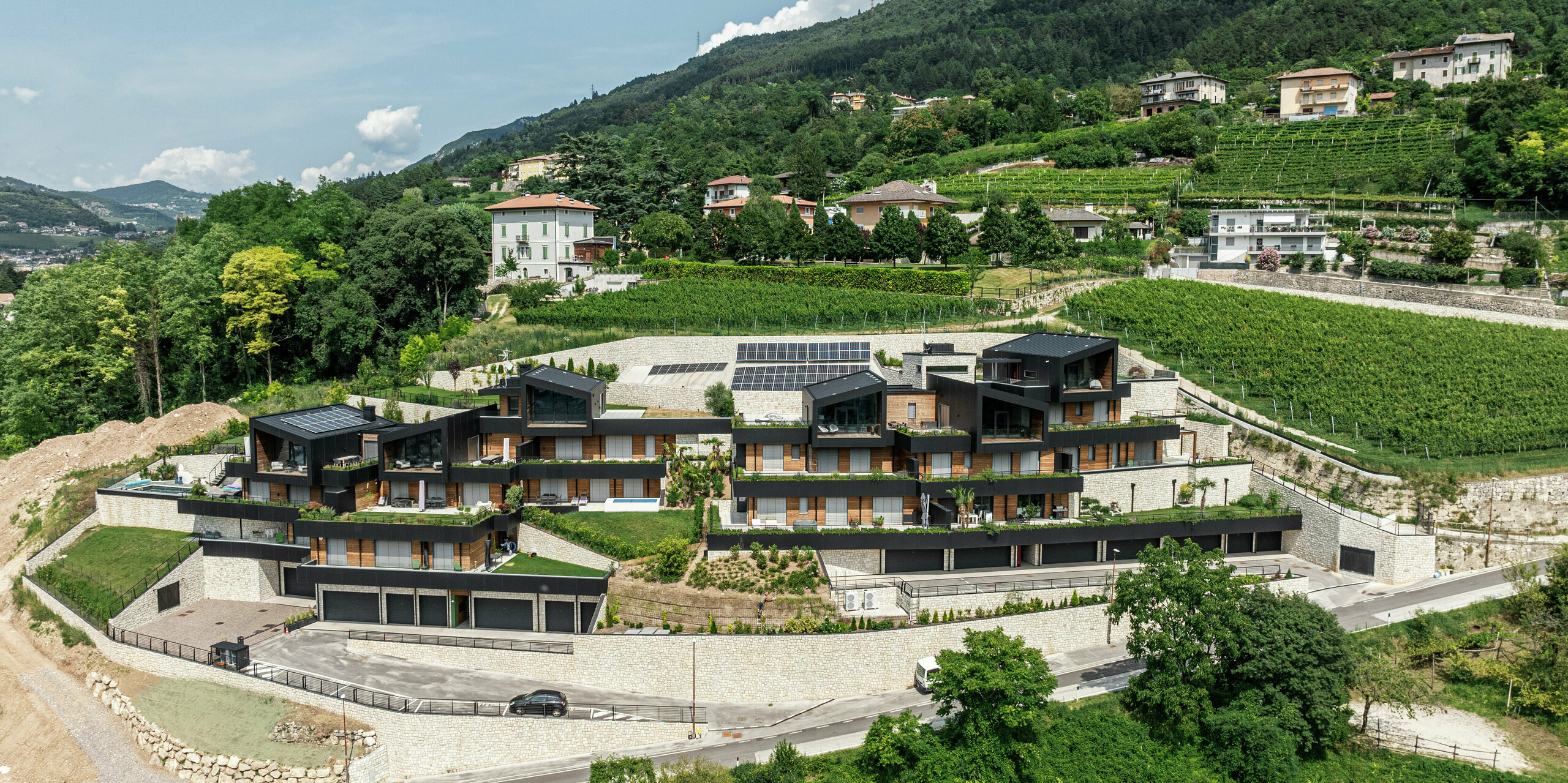 Une symbiose parfaite entre nature et architecture moderne : le complexe résidentiel exclusif à flanc de colline s'intègre harmonieusement dans les vignobles environnants de Trente. Les façades en panneaux composites en aluminium PREFA en P.10 noir et les toits PREFALZ offrent non seulement un design élégant mais également une résistance maximale aux intempéries. Des espaces verts, des installations photovoltaïques et des terrasses spacieuses soulignent le concept de vie durable. La combinaison de la pierre naturelle, du bois et de l'aluminium crée une enveloppe de bâtiment durable et nécessitant peu d'entretien avec une vue panoramique unique sur la vallée.