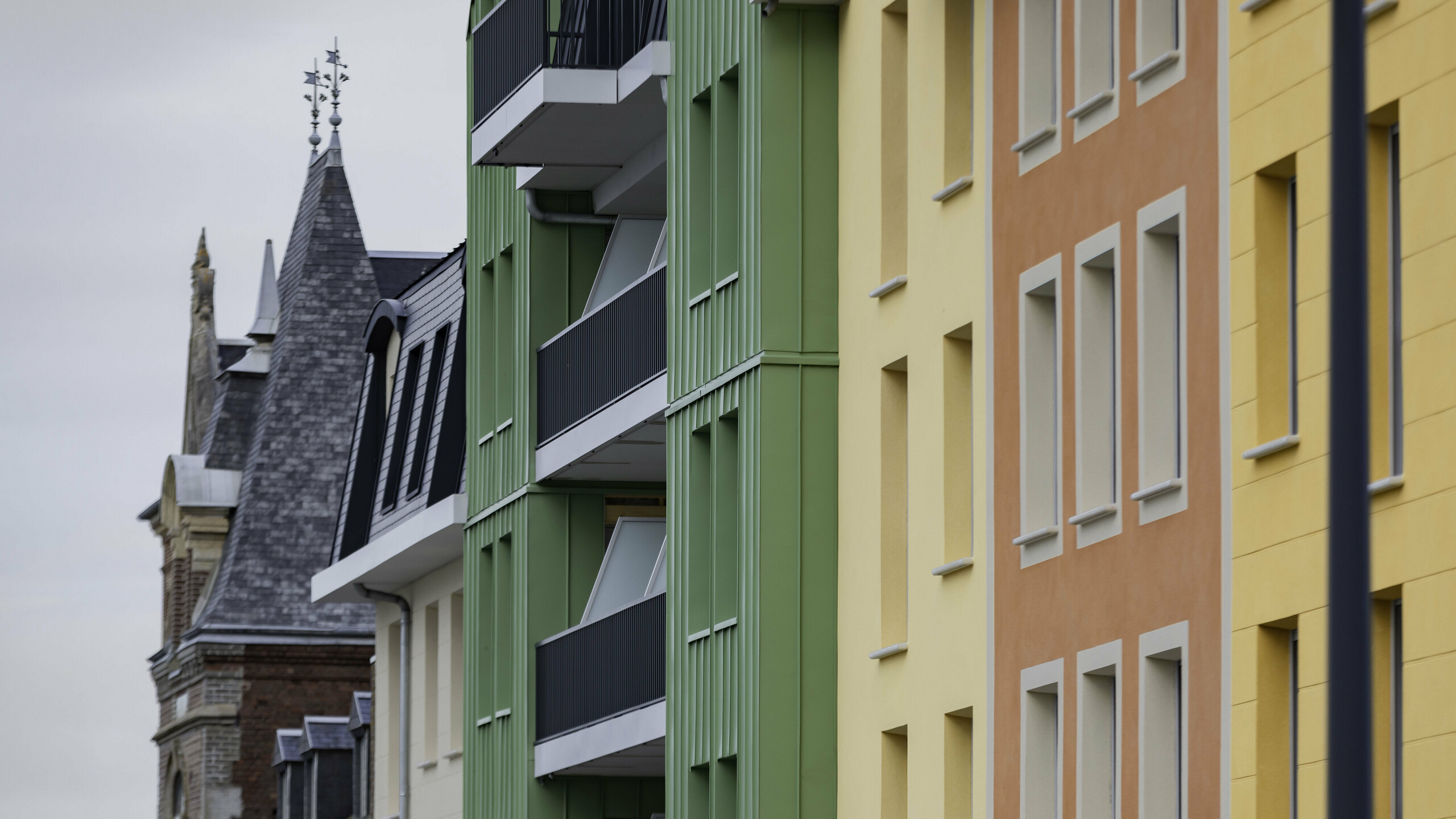 Prise de vue latérale de la résidence Le Phare à Le Tréport. On aperçoit le joint debout PREFALZ et FALZONAL dans les teintes vert olive et P.10 anthracite. S'en suivent alors des façades en crépis jaunes orangées et des toiture en ardoise.