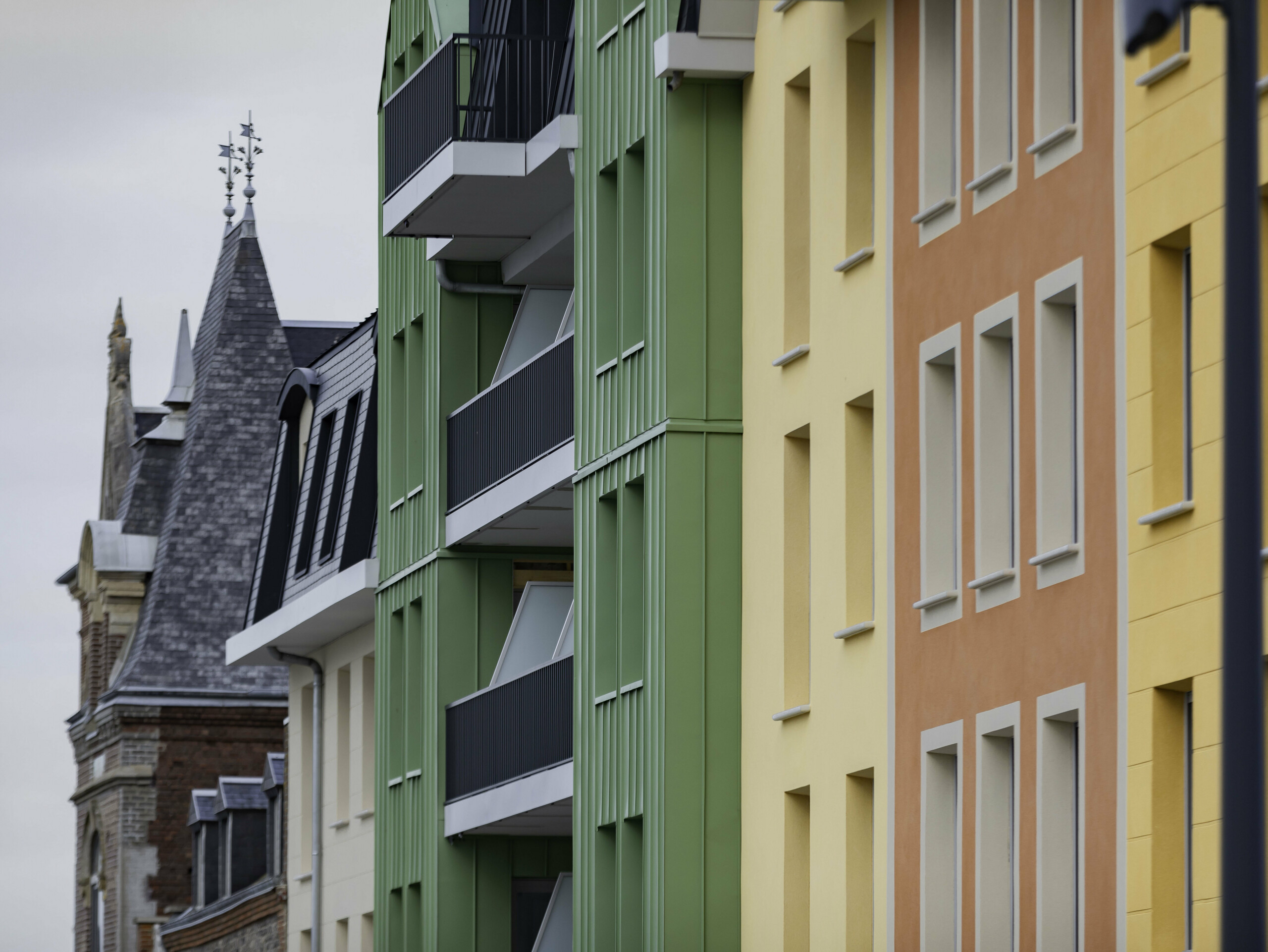 Prise de vue latérale de la résidence Le Phare à Le Tréport. On aperçoit le joint debout PREFALZ et FALZONAL dans les teintes vert olive et P.10 anthracite. S'en suivent alors des façades en crépis jaunes orangées et des toiture en ardoise.