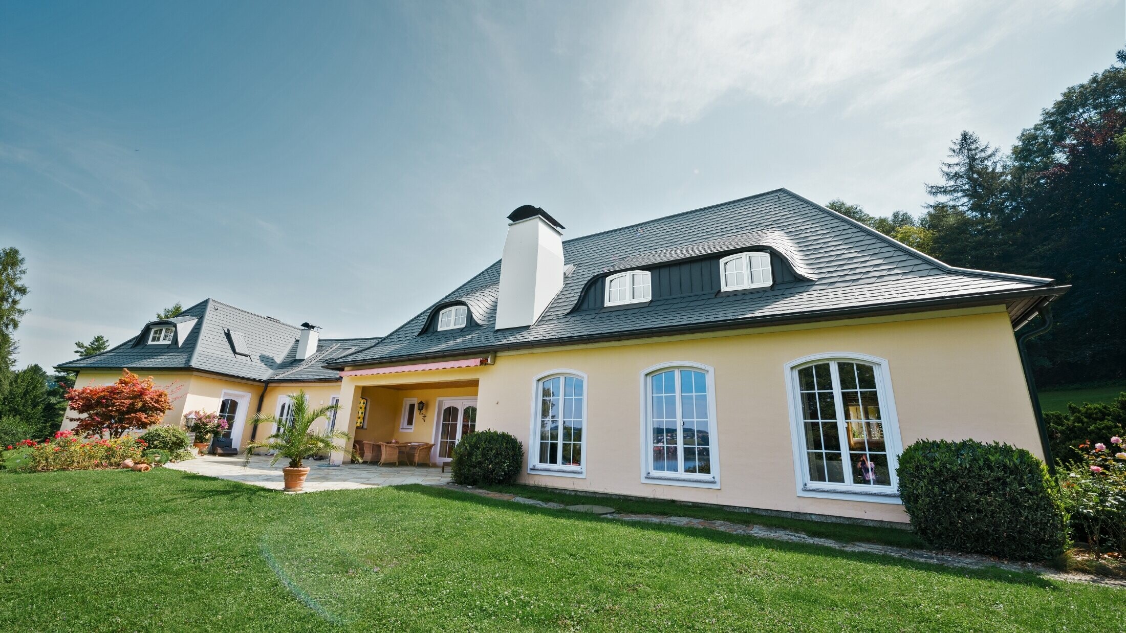 Maison individuelle classique avec lucarne arrondie, recouverte des bardeaux de toiture PREFA résistants aux tempêtes, avec garantie matériau de 40 ans.