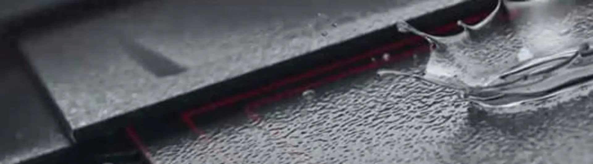 Gros plan sur les losanges de toiture PREFA avec gouttes d’eau sur la surface. Surface stucco pour les tuiles et couleur anthracite. 