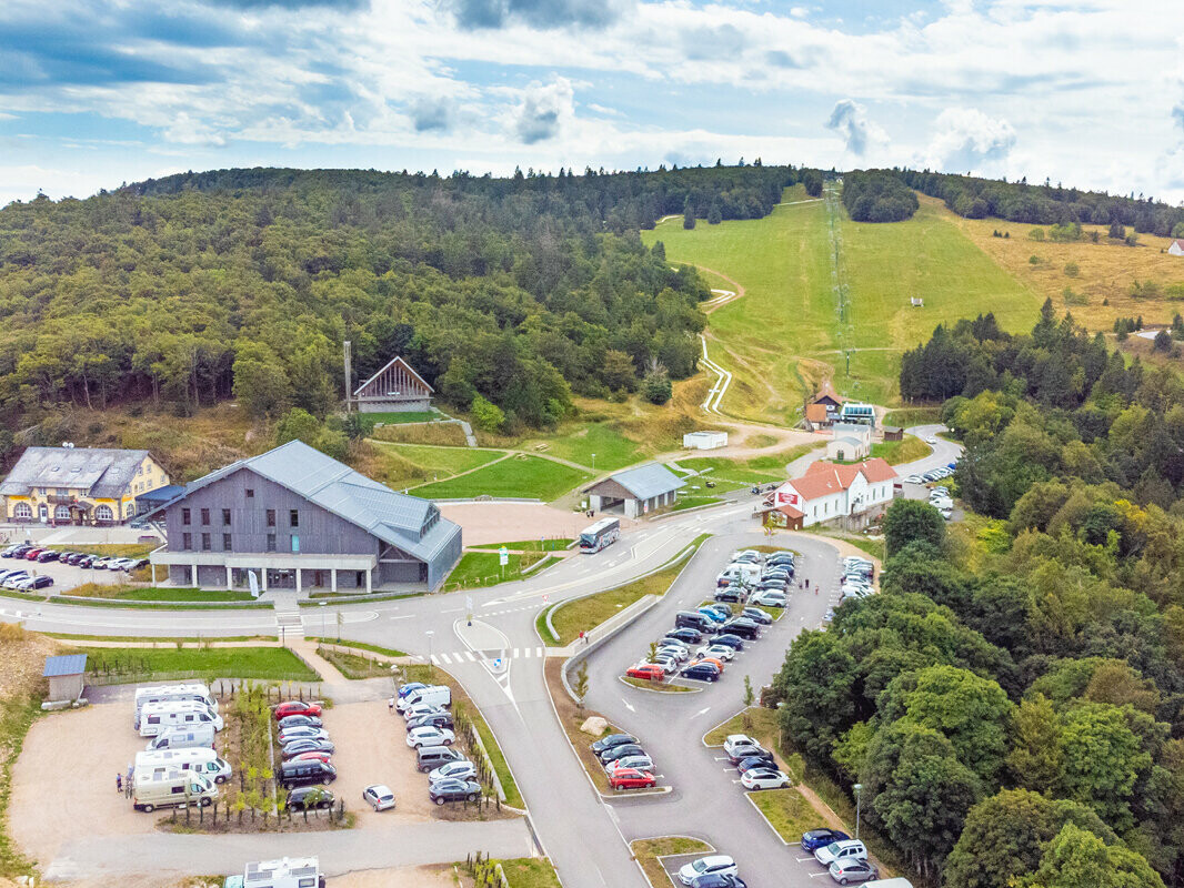 Prise de vue de drone de la chapelle du Col de la Schlucht, rénovée avec les bardeaux en aluminium PREFA dans la teinte P.10 gris souris. La photographie permet de voir la localisation dans son ensemble, avec une partie des Vosges et un large parking.
