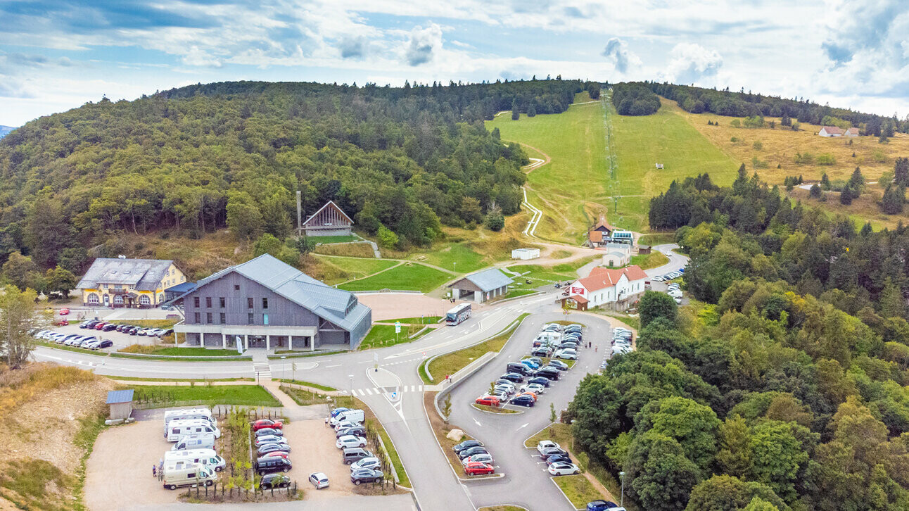 Prise de vue de drone de la chapelle du Col de la Schlucht, rénovée avec les bardeaux en aluminium PREFA dans la teinte P.10 gris souris. La photographie permet de voir la localisation dans son ensemble, avec une partie des Vosges et un large parking.