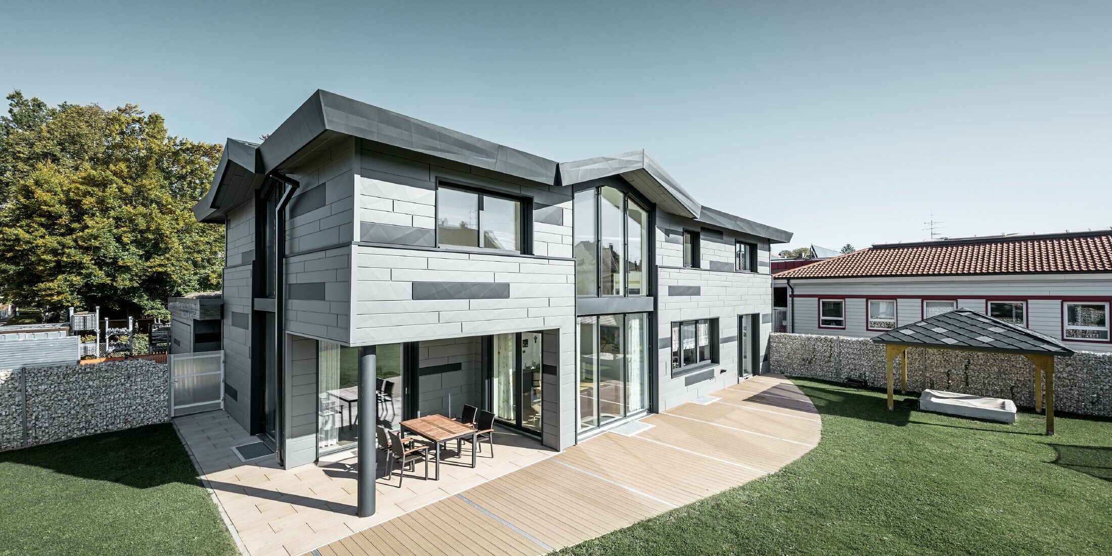 Cette maison individuelle moderne située à Türkheim est équipée des panneaux de façade PREFA FX.12 dans les couleurs P.10 gris souris et anthracite. La photo montre une partie du jardin.