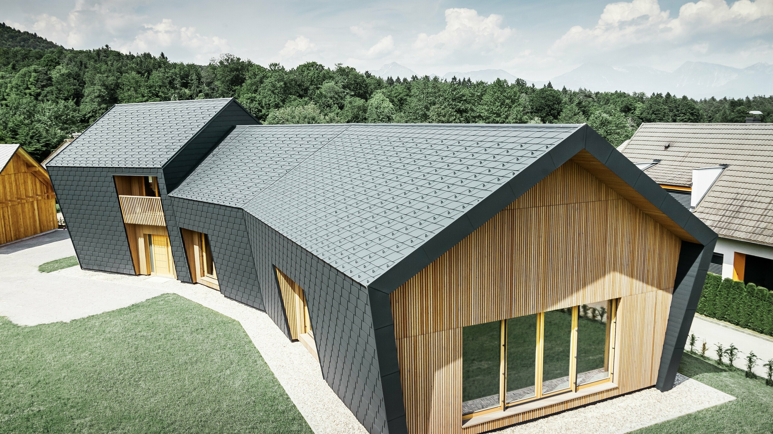 Grandes surfaces de toiture ou de façade, recouvertes des bardeaux de toiture DS.19 en P.10 anthracite, l'extrémité de la façade a été revêtue de bois