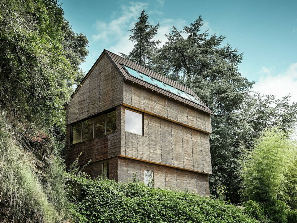 Maison dans l'ouest de la France avec toiture en bardeaux PREFA couleur P.10 brun noisette, située sur une colline escarpée - design moderne avec façade en bois de saule et toiture économe en énergie.