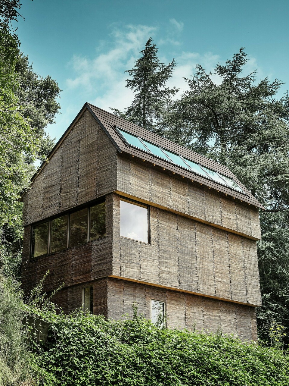 Maison dans l'ouest de la France avec toiture en bardeaux PREFA couleur P.10 brun noisette, située sur une colline escarpée - design moderne avec façade en bois de saule et toiture économe en énergie.