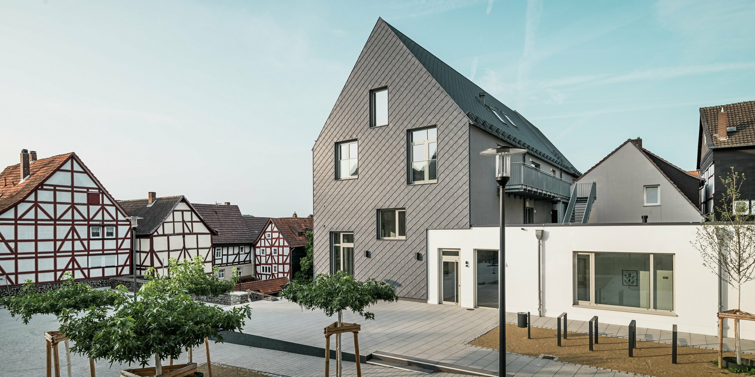 Vue arrière du Volkshaus modernisé à Homberg, DE, avec losanges de façade 29x29 PREFA en P.10 gris pierre. La façade élégante allie un design moderne aux maisons à colombages historiques de la région et offre une protection contre les intempéries, une durabilité et une esthétique intemporelle.