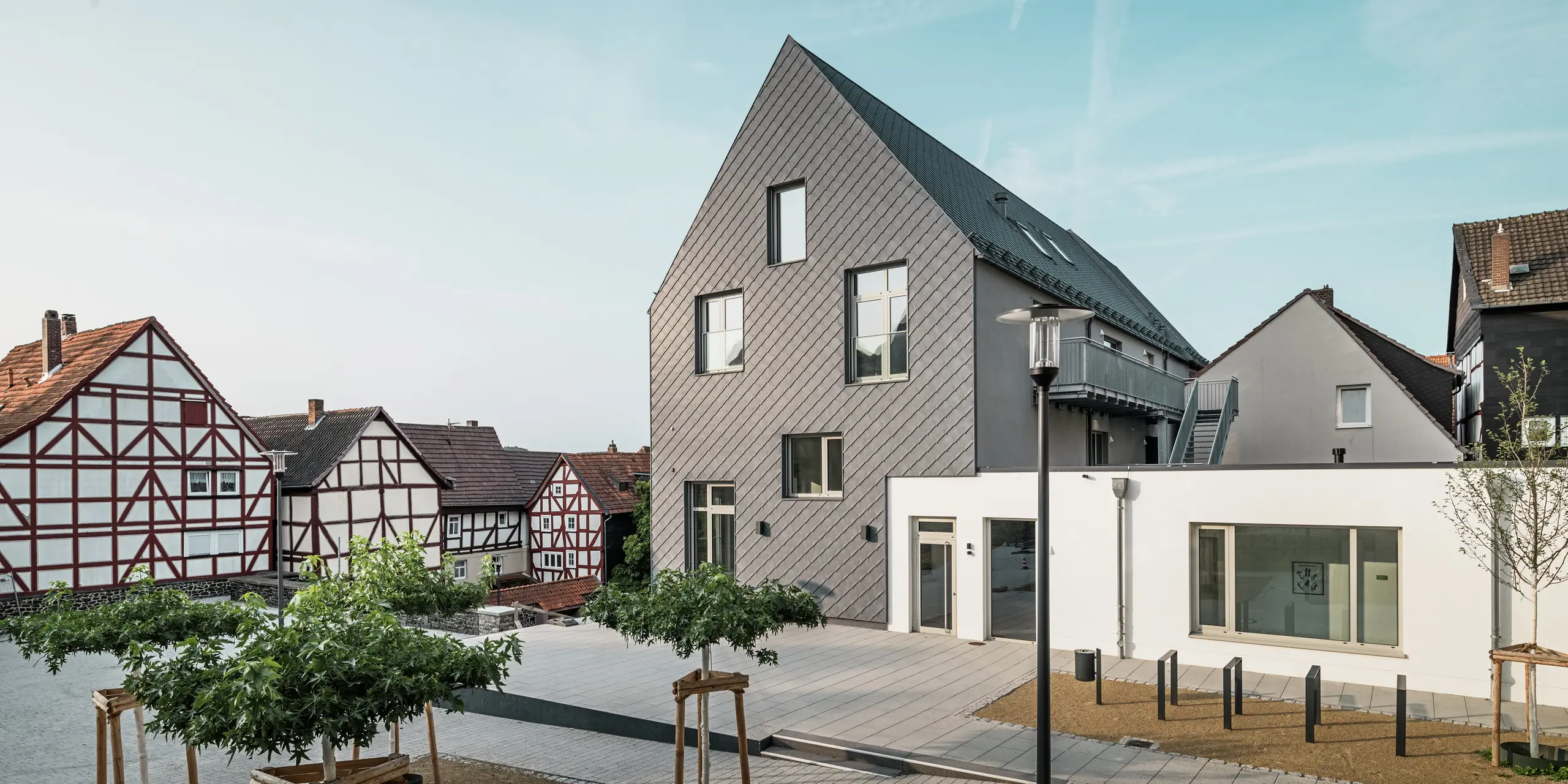 Vue arrière du Volkshaus modernisé à Homberg, DE, avec losanges de façade 29x29 PREFA en P.10 gris pierre. La façade élégante allie un design moderne aux maisons à colombages historiques de la région et offre une protection contre les intempéries, une durabilité et une esthétique intemporelle.