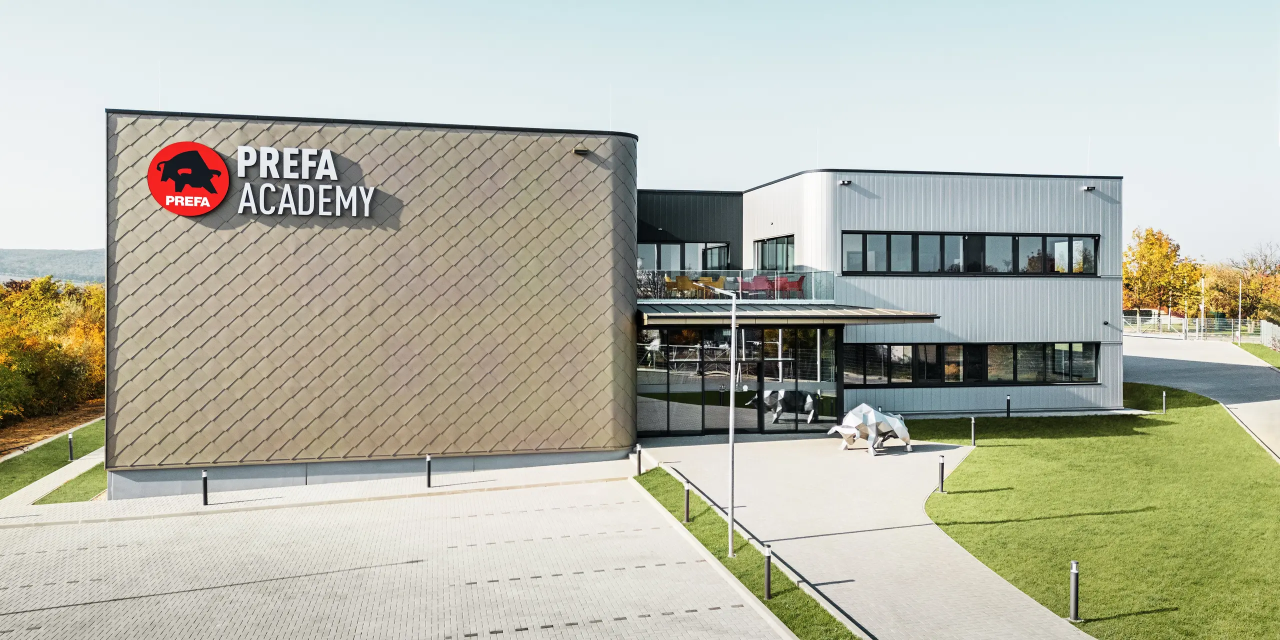 Le nouveau site de PREFA Hongrie à Törökbálint impressionne par sa façade moderne composée de losanges de façade PREFA 44 × 44 en bronze et de Sidings PREFA en argent métallisé. Les produits en aluminium durables garantissent une enveloppe de bâtiment résistante aux intempéries, facile d'entretien et visuellement attrayante. Le logo PREFA frappant et la sculpture du taureau en aluminium soulignent la puissance d'innovation, la qualité et la force de l'entreprise.