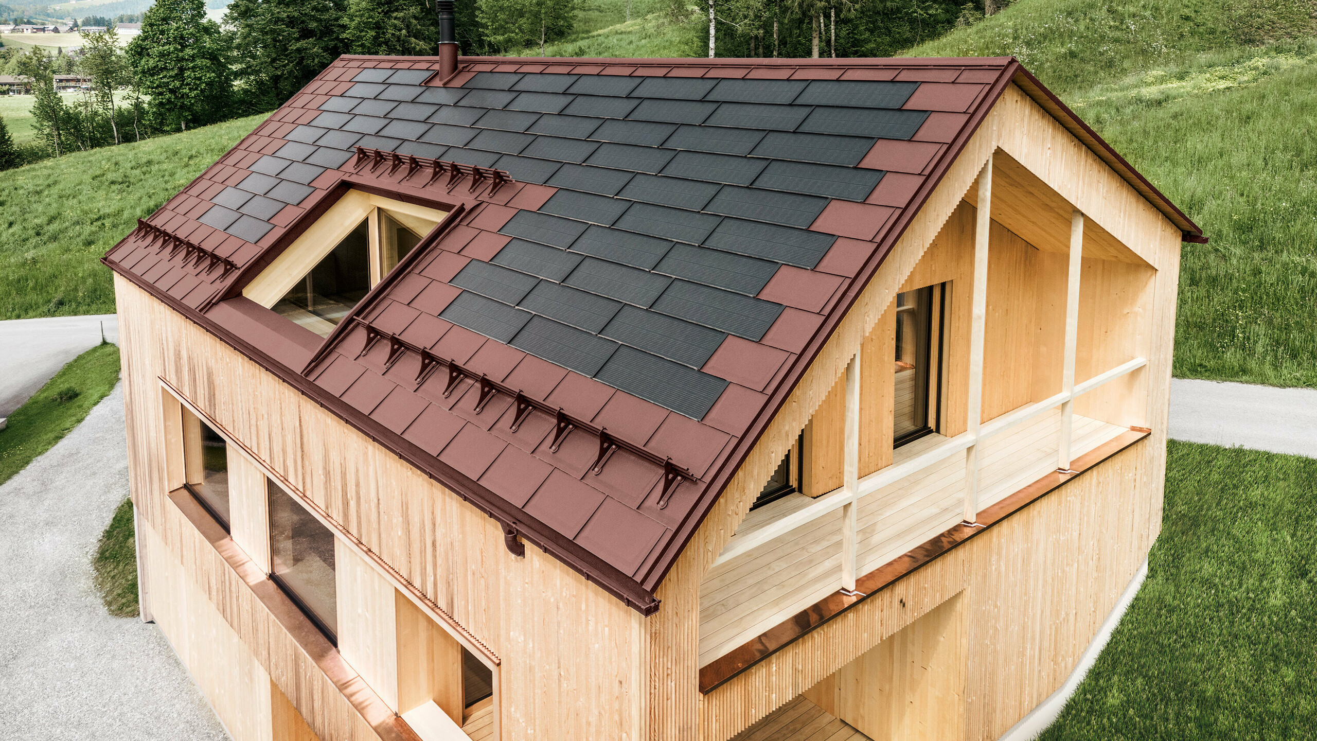 Maison individuelle située dans la localité autrichienne d'Egg, avec le panneau solaire de toiture PREFA et le panneau de toiture R.16 en rouge oxydé, combinés à une façade en bois