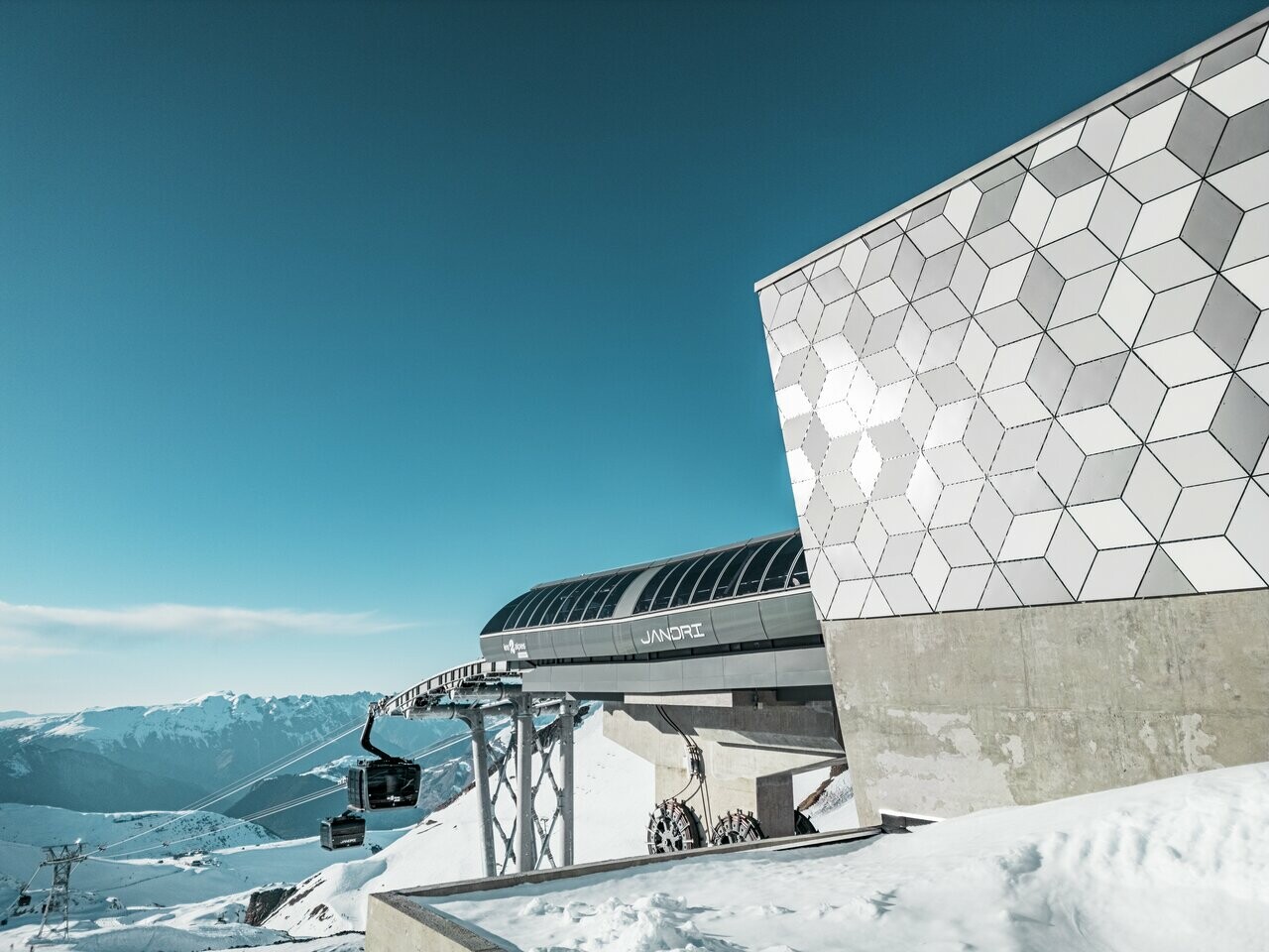 Vue rapprochée de la façade d'une station du nouveau téléphérique Le Jandri de la station Les 2 Alpes, recouverte de panneaux composites en aluminium PREFABOND façonné en losanges de trois couleurs différentes : blanc Prefa, blanc pur et argent fumé.
