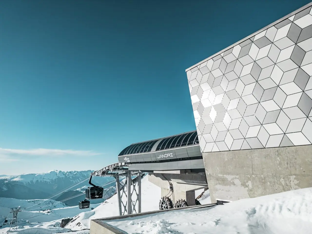Vue rapprochée de la façade d'une station du nouveau téléphérique Le Jandri de la station Les 2 Alpes, recouverte de panneaux composites en aluminium PREFABOND façonné en losanges de trois couleurs différentes : blanc Prefa, blanc pur et argent fumé.