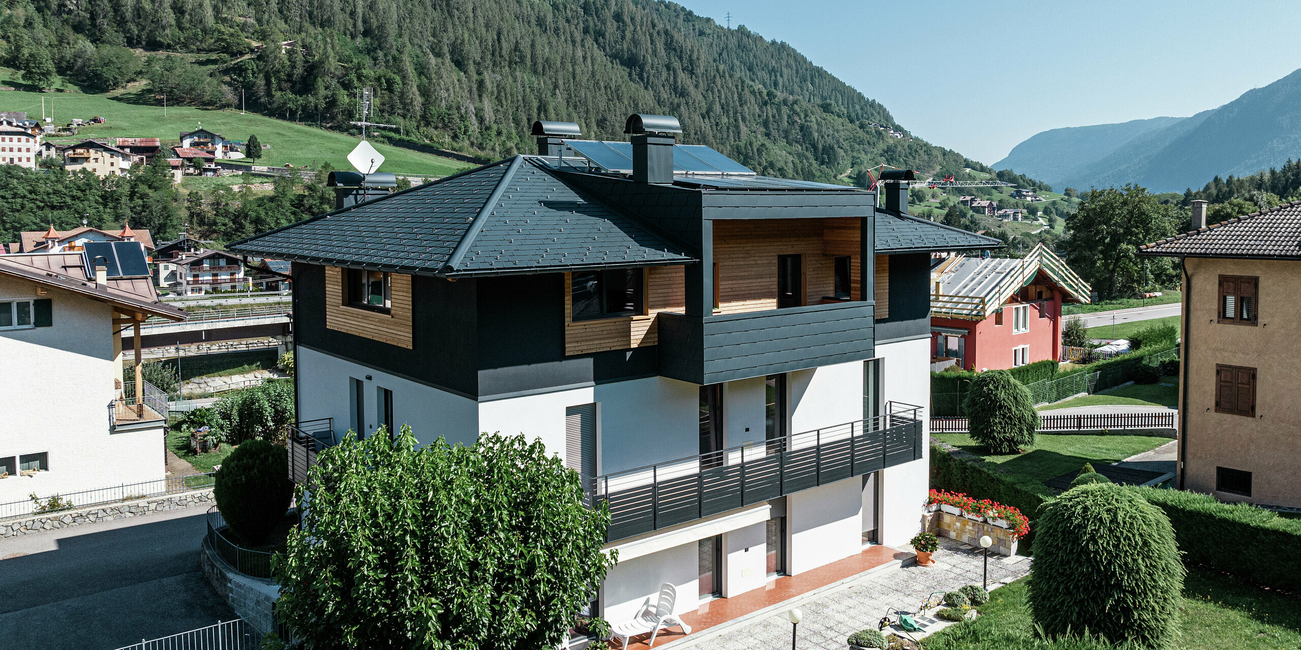 Vue aérienne de l'immeuble résidentiel de Commezzadura avec les DS.19 PREFA en P.10 anthracite. Certaines parties de la façade du grenier ont été revêtues de bois, créant ainsi une impression d'ensemble harmonieuse. Les balcons couverts sont également recouverts d'un produit en aluminium de haute qualité.