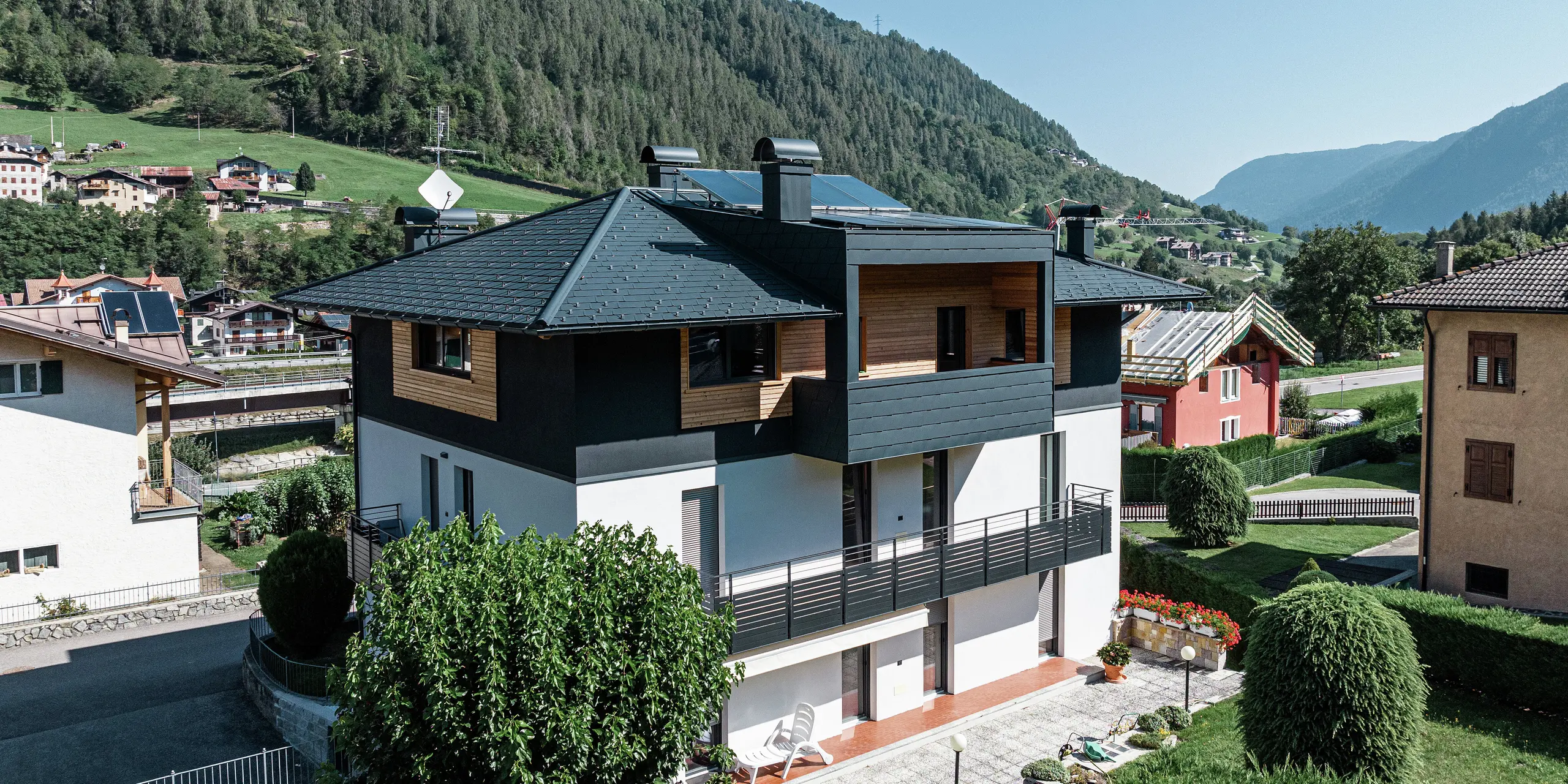 Vue aérienne de l'immeuble résidentiel de Commezzadura avec les DS.19 PREFA en P.10 anthracite. Certaines parties de la façade du grenier ont été revêtues de bois, créant ainsi une impression d'ensemble harmonieuse. Les balcons couverts sont également recouverts d'un produit en aluminium de haute qualité.