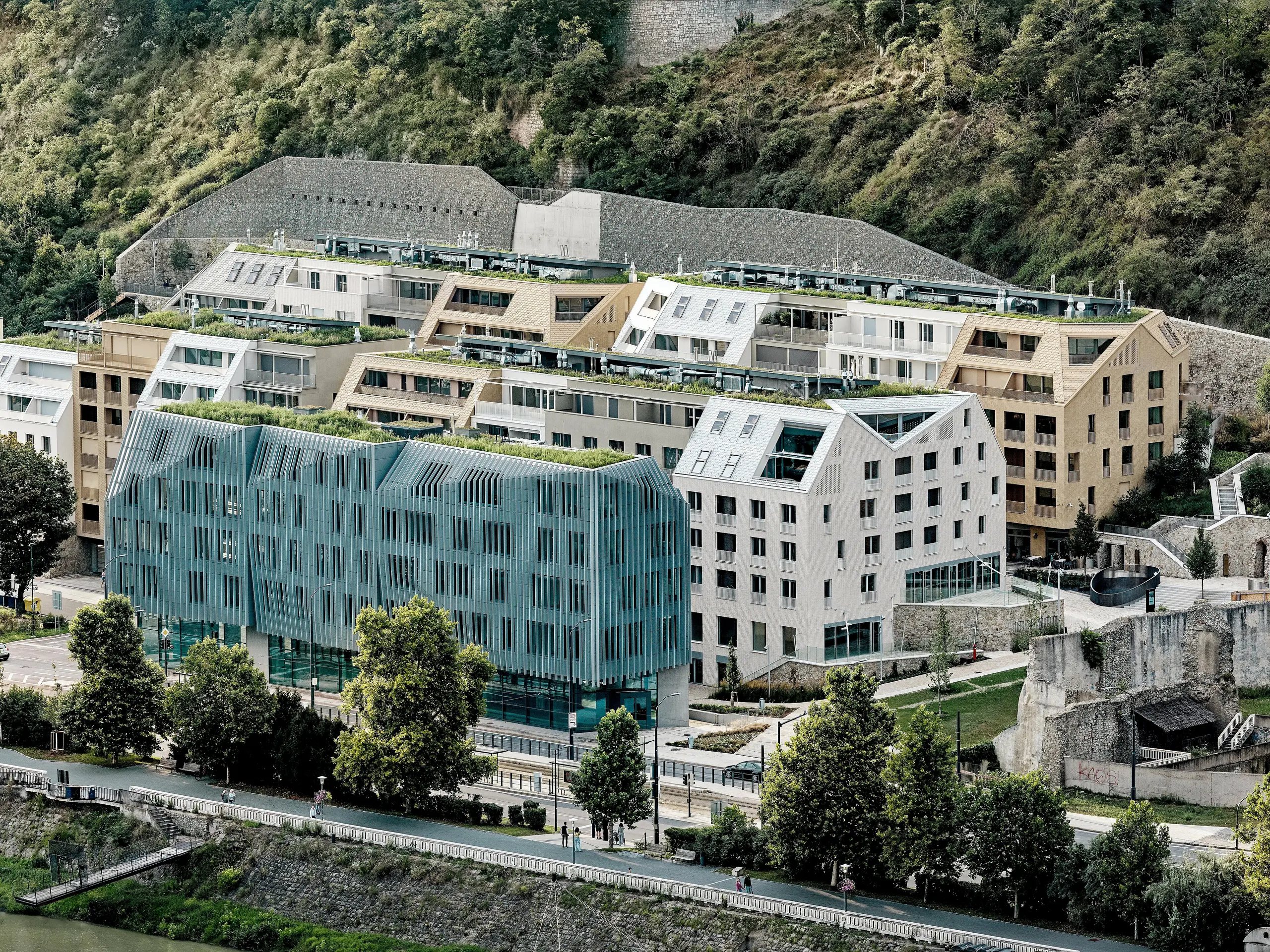 Le quartier urbain de Vydrica à Bratislava, sur les rives du Danube, offre un panorama impressionnant : l’architecture en terrasses, avec ses toitures végétalisées, ses toits à forte pente et ses lignes épurées, est mise en valeur par les tuiles de toiture en aluminium PREFA, disponibles en blanc, brun sable et bronze. La variété des toitures, agrémentée de puits de lumière intégrés et de détails soignés, attire le regard sur l’ensemble. L’aluminium PREFA permet de réaliser des formes délicates et complexes et séduit par sa durabilité, sa légèreté et son extrême résistance aux intempéries – un matériau idéal pour les projets urbains durables et architecturalement sophistiqués.