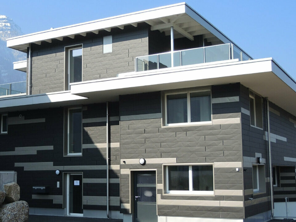 Modernes Gebäude in der Schweiz mit Bergen im Hintergrund mit einer neuen PREFA Siding.X Fassade; Die Alu-Paneele wurden in zwei unterschiedlichen Farben montiert, daraus ergibt sich ein individuelles Fassadendesign.