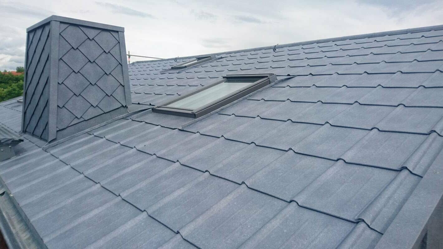 Vue détaillée d’une rénovation de toiture à l’aide de tuiles PREFA couleur P.10 gris pierre, habillage de la cheminée inclus