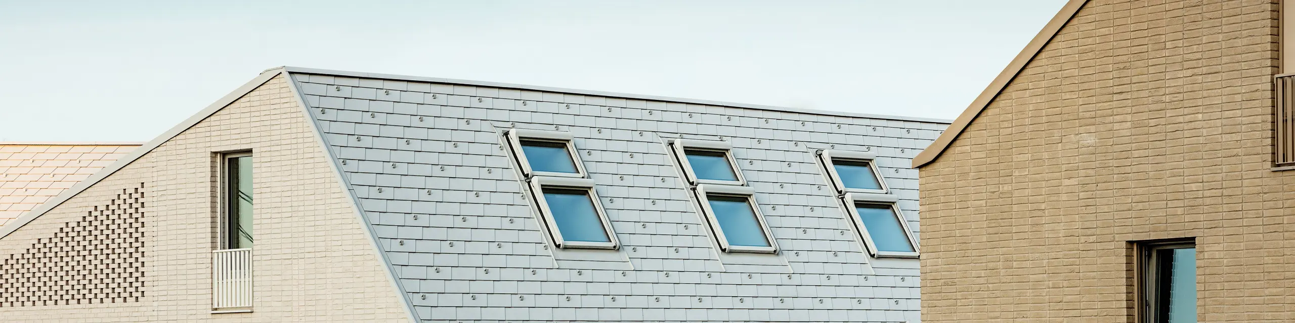 Toitures remarquables dans le nouveau quartier urbain de Vydrica à Bratislava : les toits à forte pente, recouverts de tuiles en aluminium PREFA P.10 blanc Prefa posées avec précision, créent des accents saisissants grâce à leurs lignes épurées et leurs puits de lumière disposés de façon rythmée. La surface homogène unifie la toiture et la façade en un ensemble élégant et fait écho au style architectural serein de la vieille ville. L’aluminium PREFA séduit par sa légèreté, sa grande stabilité, son extrême résistance aux intempéries et sa qualité durable et nécessitant peu d’entretien – idéal pour les solutions de toiture complexes et exigeantes sur le plan architectural.