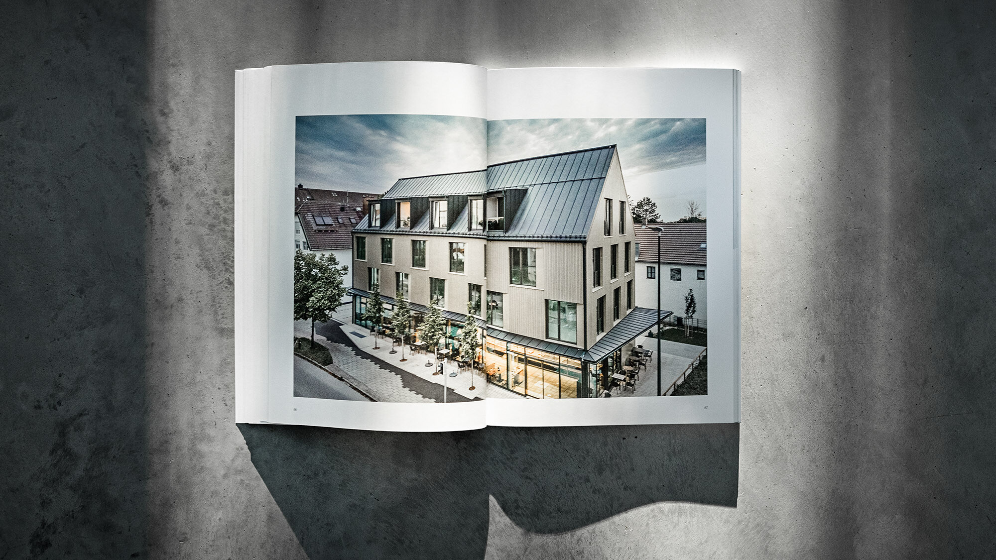 Le livre PREFARENZEN 2024 ouvert et sur fond gris avec une double page illustrant l'immeuble résidentiel et commercial à Feldkirchen du cabinet d'architectes Heigl.