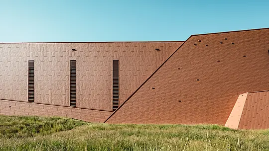 La station de pompage d'eau potable de Lottum (Pays-Bas) s'intègre harmonieusement à son environnement naturel, telle une sculpture architecturale. La façade en aluminium PREFA Siding.X, d'une teinte rouille chaleureuse, contraste de façon saisissante avec la verdure des prairies et des collines environnantes, et séduit par sa surface finement texturée et vibrante. D'élégantes ouvertures verticales apportent une touche de précision. Durables, légers et entièrement recyclables, les panneaux en aluminium PREFA impressionnent par leur haute résistance aux intempéries, leur inaltérabilité des couleurs et leur capacité à constituer une enveloppe de bâtiment durable et nécessitant peu d'entretien. Cette station de pompage d'eau potable constitue ainsi un fleuron architectural dans le domaine des infrastructures.