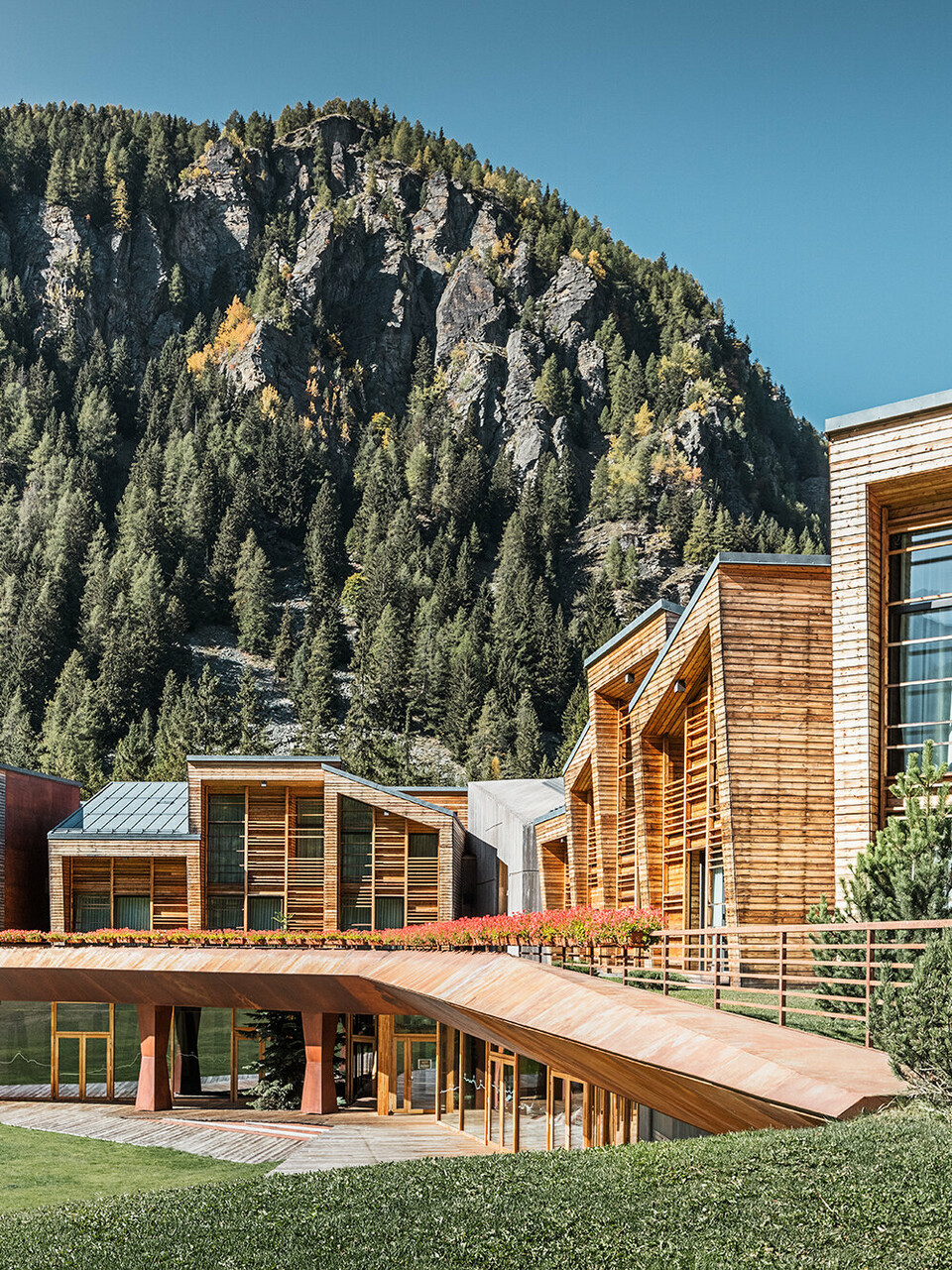 Seitenansicht des oberen und unteren Bereichs des CampZero Resorts im Aostatal mit Gebirge im Hintergrund.