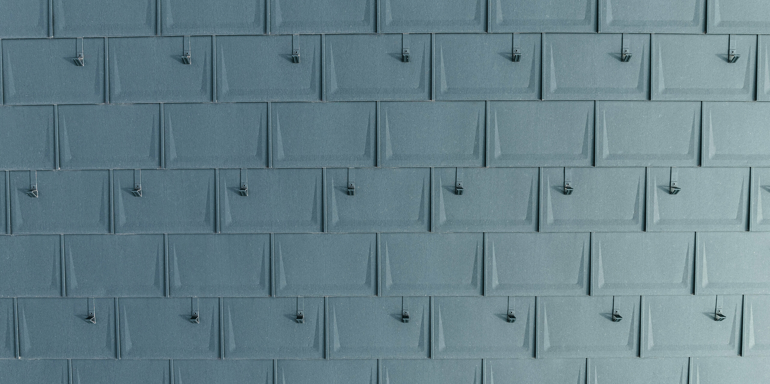 Vue détaillée des PREFA R.16 posés avec précision en P.10 anthracite avec arrêts de neige montés. Le panneau de toit linéaire en aluminium impressionne par son aspect moderne, sa durabilité et sa résistance extrême aux intempéries. Grâce à une technologie de fixation sophistiquée, il est particulièrement résistant aux tempêtes et aux cassures. Les butées à neige offrent une sécurité supplémentaire dans les régions enneigées et empêchent les masses de neige de glisser de manière incontrôlable.