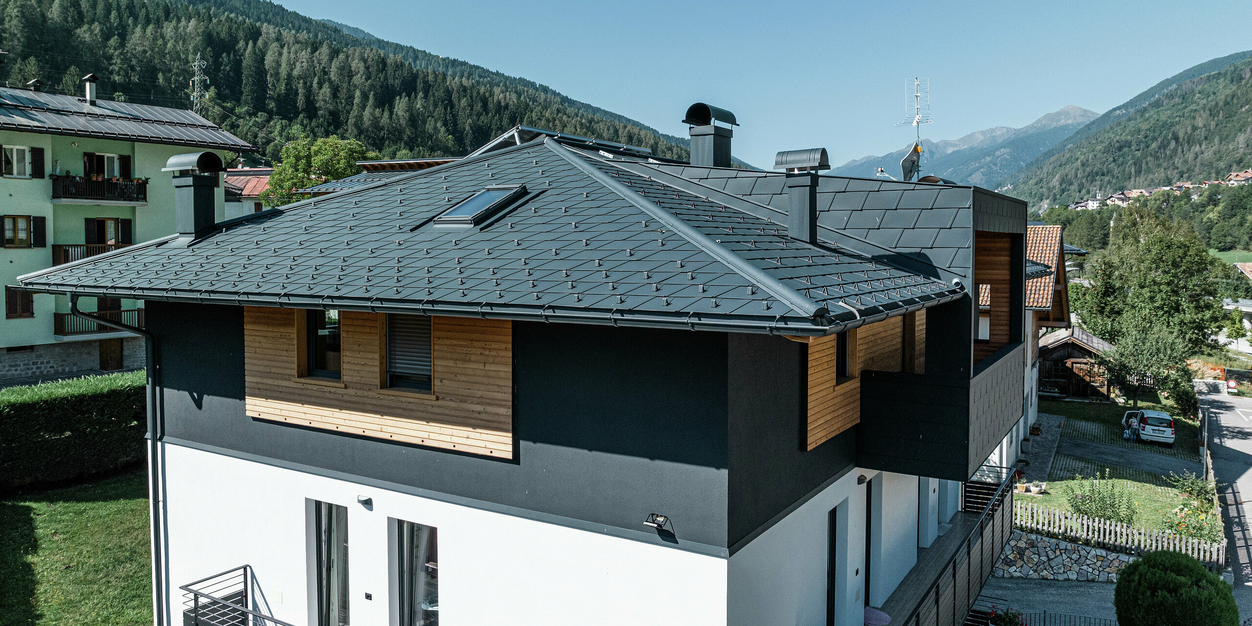 Vue du dernier étage de l'immeuble résidentiel de Commezzadura avec les DS.19 PREFA en P.10 anthracite et façade en bois. La toiture en tôle de haute qualité protège le bâtiment des conditions climatiques alpines.
