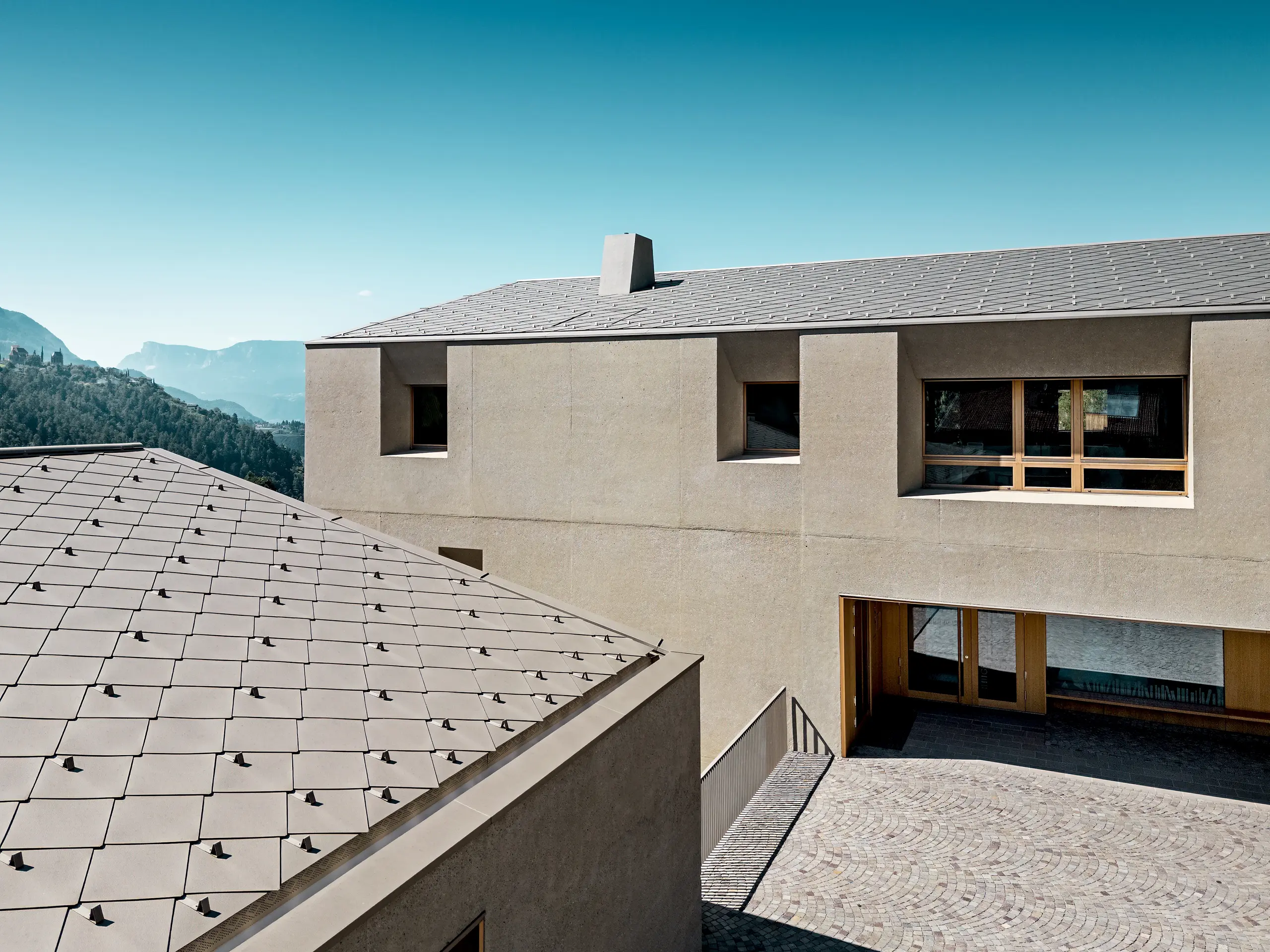Vue détaillée du centre éducatif de Riffian, doté d’une toiture en losanges PREFA 44 × 44, coloris Bronze P.10. Ce revêtement en aluminium, posé avec précision sur des volumes architecturaux aux lignes épurées, souligne le caractère moderne de la construction, assure une protection durable contre les intempéries et s’intègre harmonieusement au paysage montagneux naturel du Tyrol du Sud.