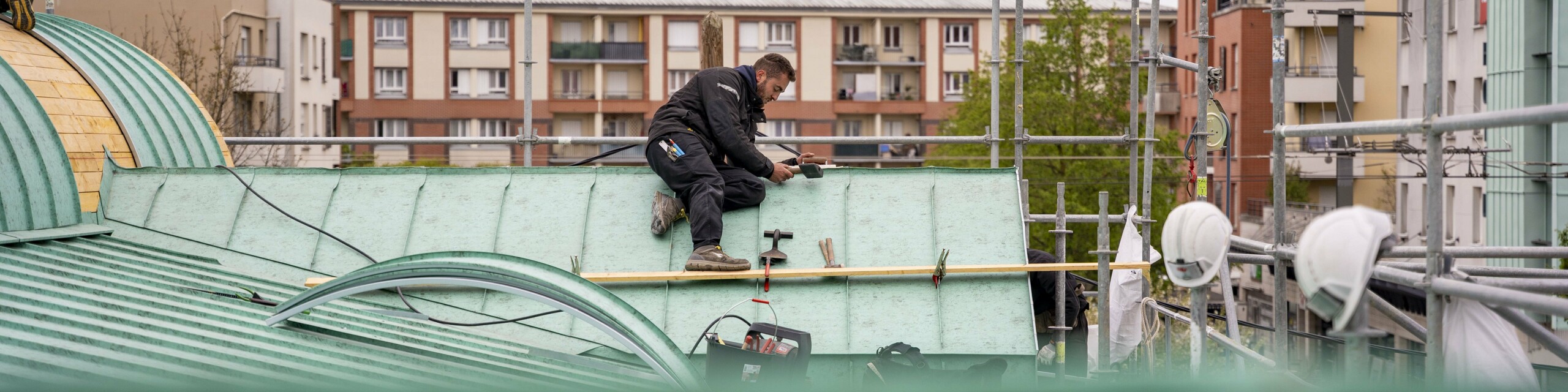 Prise de vue depuis le toit en cours de réalisation. Dans le fond, on voit un couvreur assis sur le toit, en train d'agrafer l'aluminium PREFA.