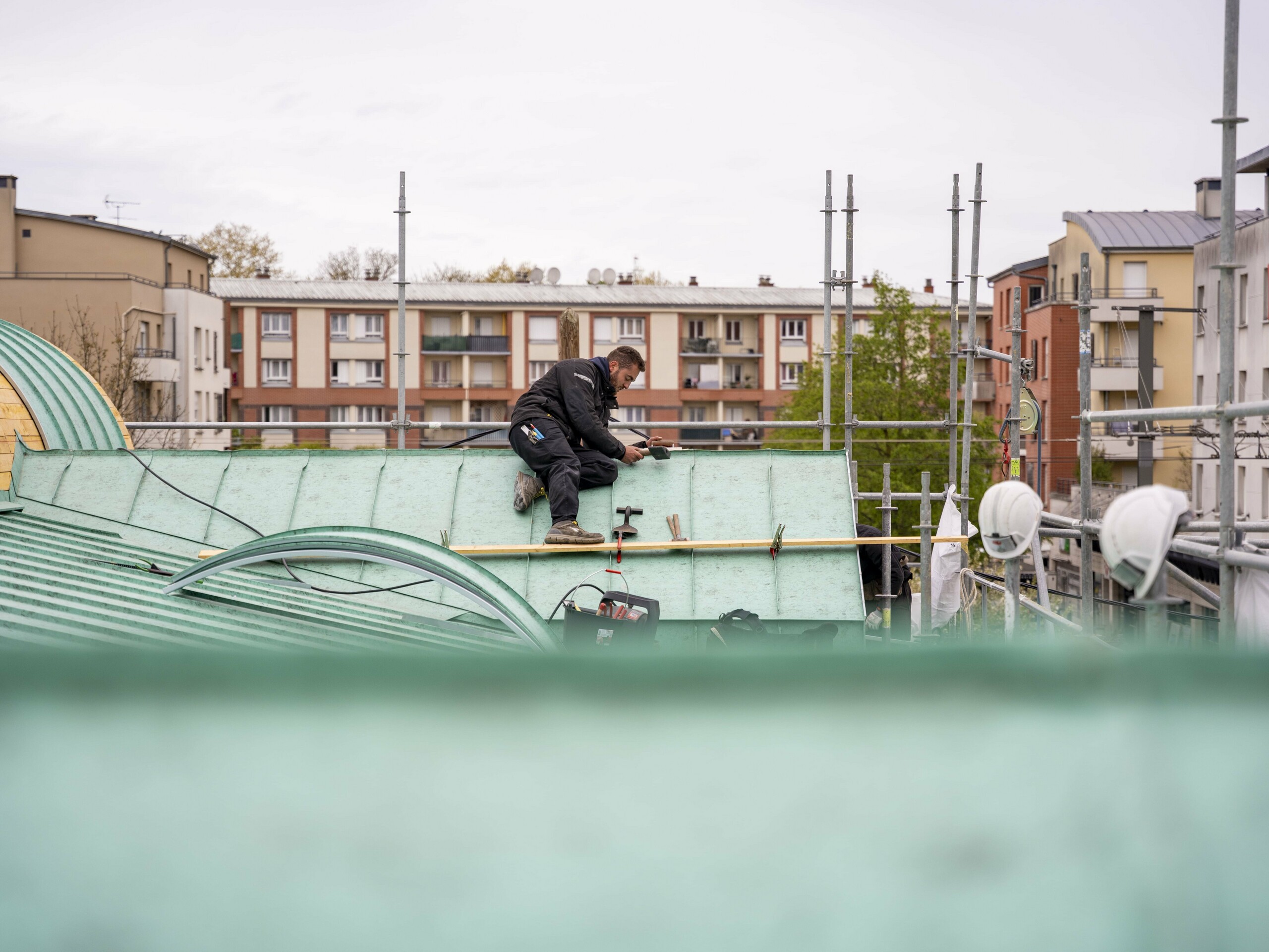 Prise de vue depuis le toit en cours de réalisation. Dans le fond, on voit un couvreur assis sur le toit, en train d'agrafer l'aluminium PREFA.
