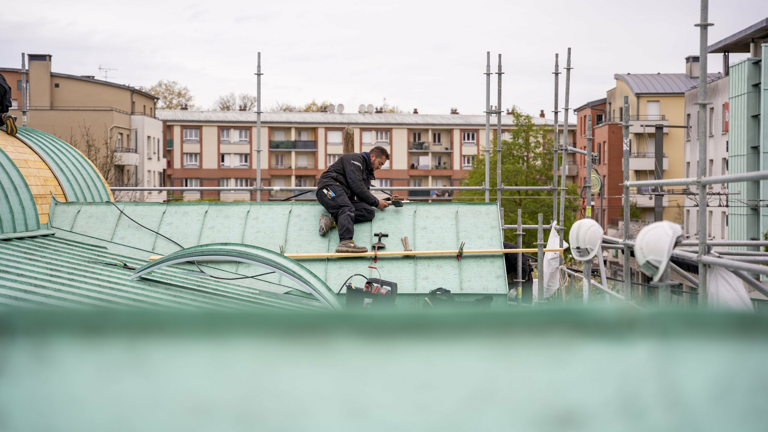 Prise de vue depuis le toit en cours de réalisation. Dans le fond, on voit un couvreur assis sur le toit, en train d'agrafer l'aluminium PREFA.